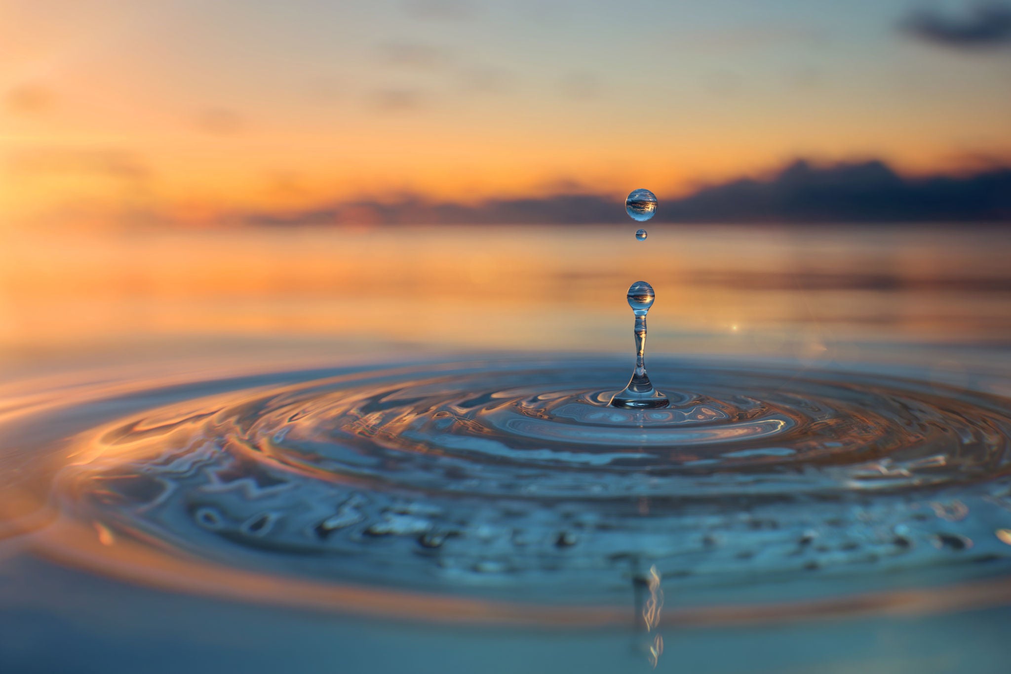 Clear Blue Water drop with circular waves on sunset background