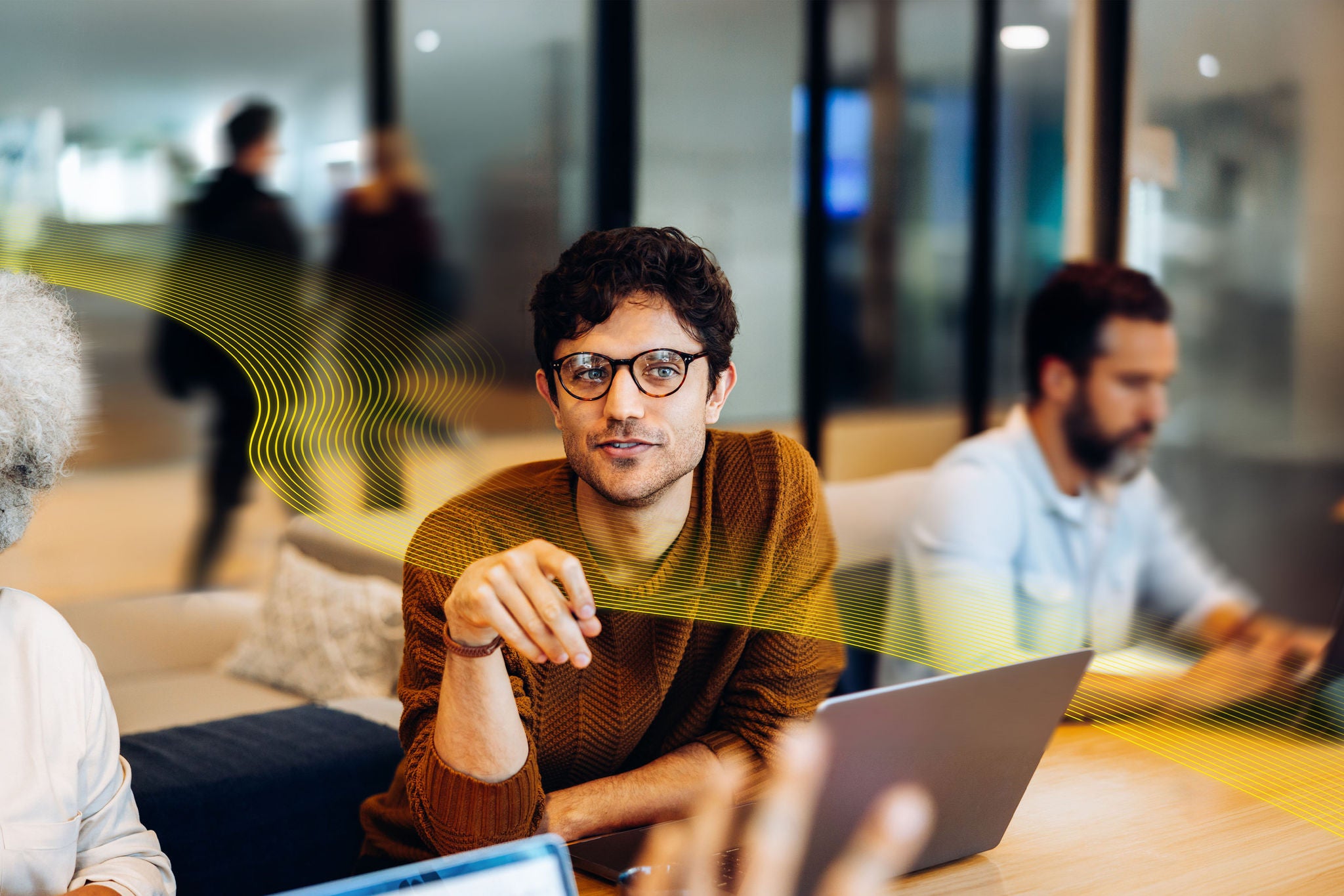 A young man leans forward as he explains his idea, using thoughtful gestures while teammates listen across the collaborative workspace.
