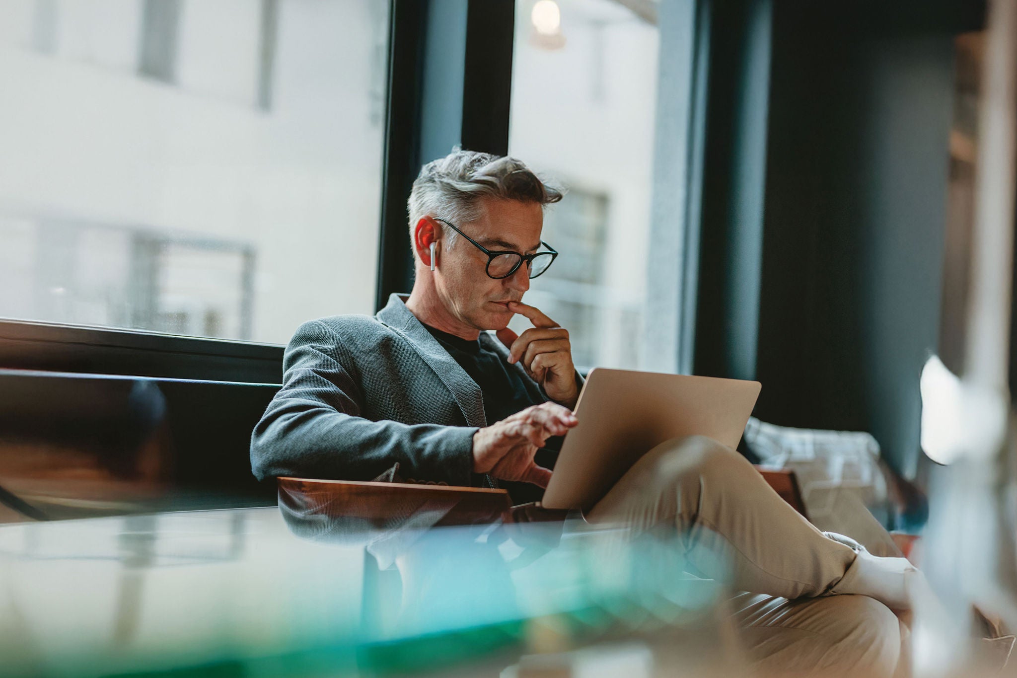 Businessman looking at laptop and thinking. Businessman reading emails on laptop in office lobby.