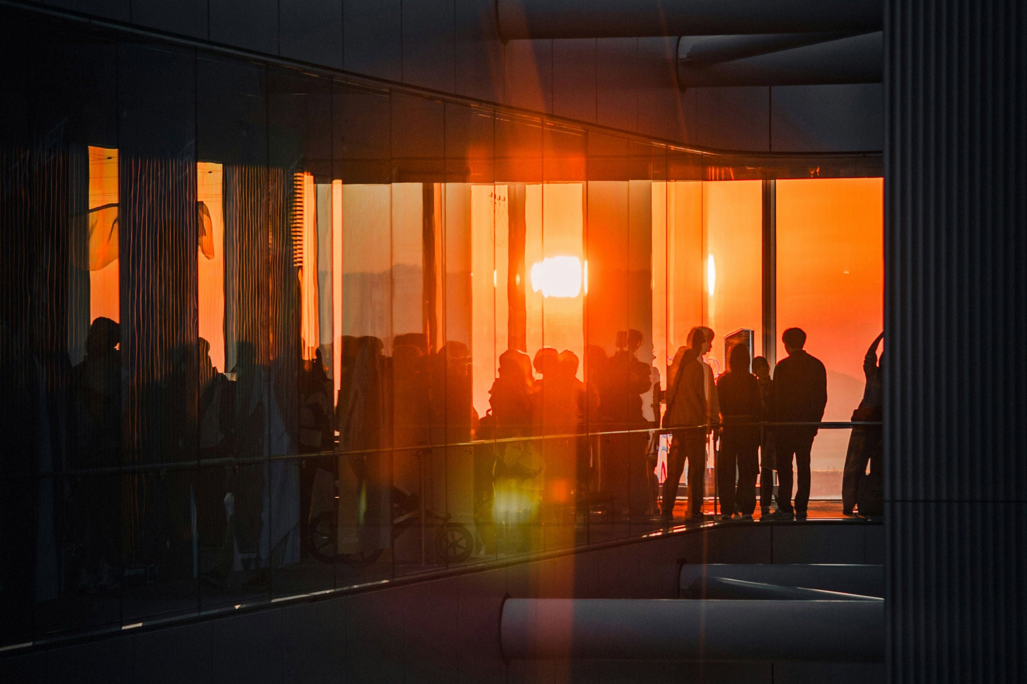 People walking on a pedestrian bridge next to a modern glass building with reflections