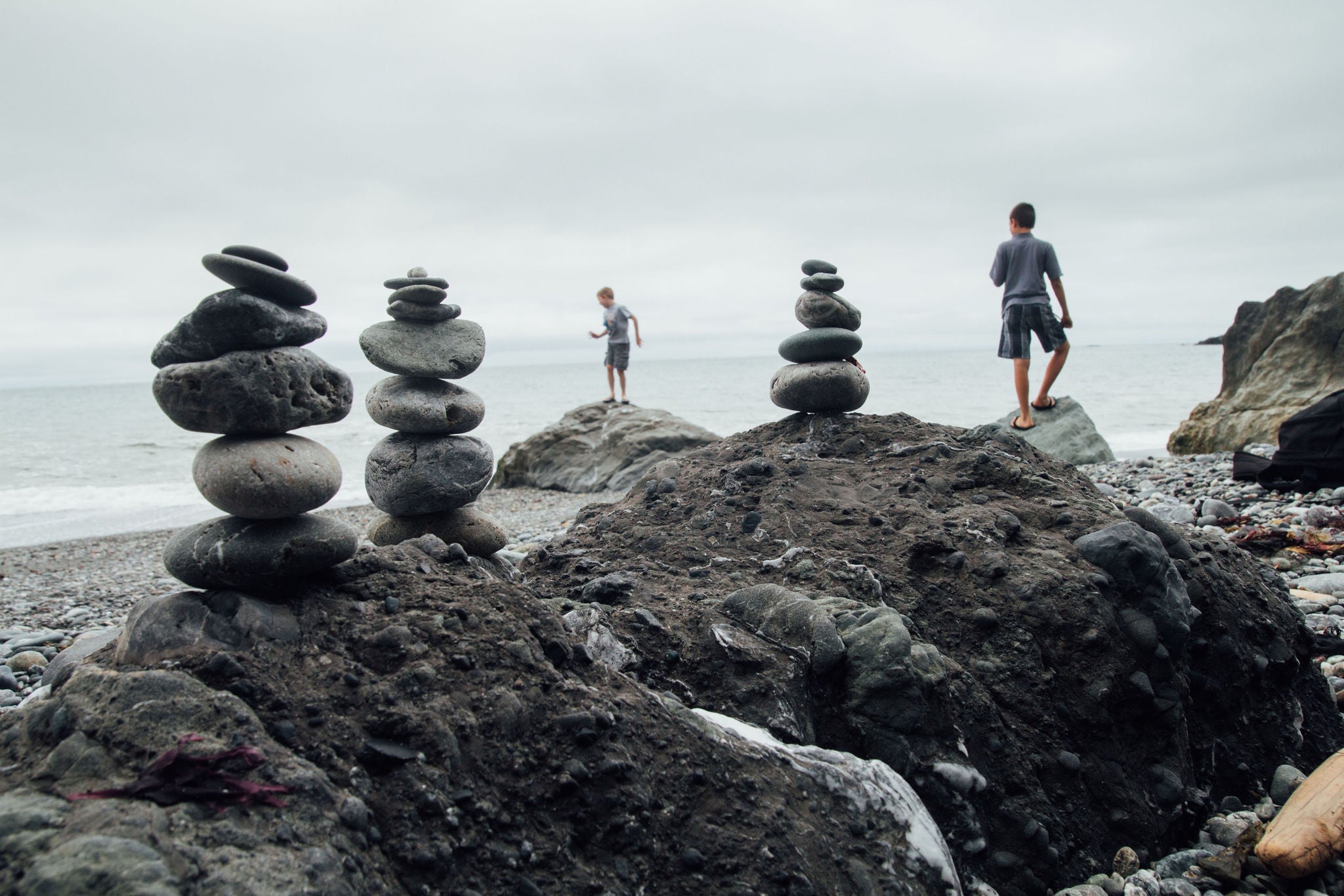 two boys walk on the beach with balanced stone towers in the forground