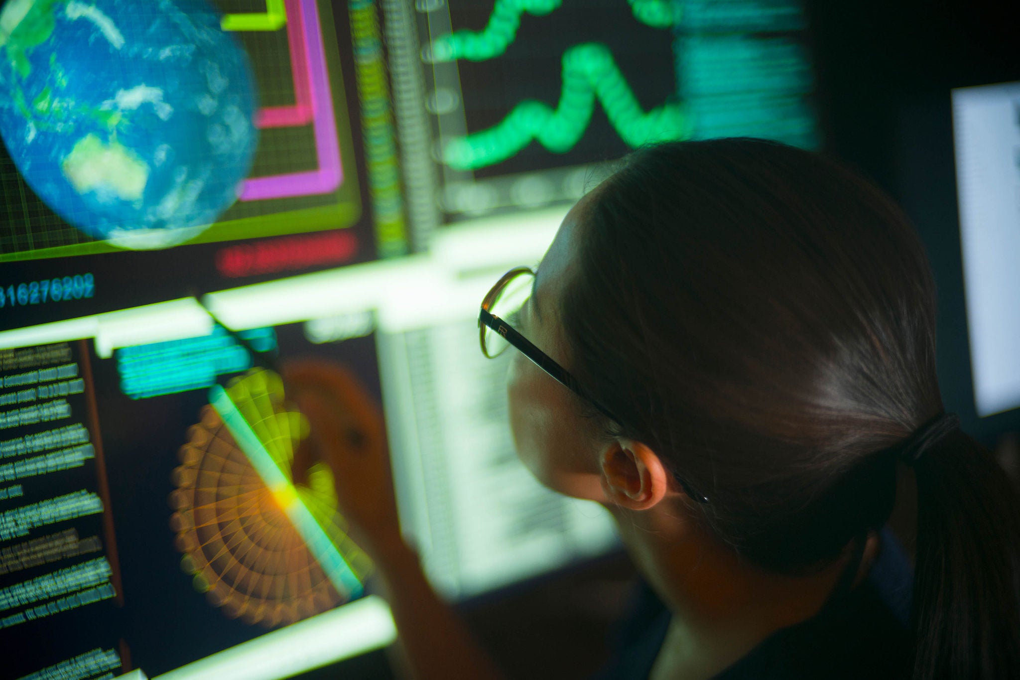 Close up stock photo of an Asian woman carefully studying global data on her large computer screen.