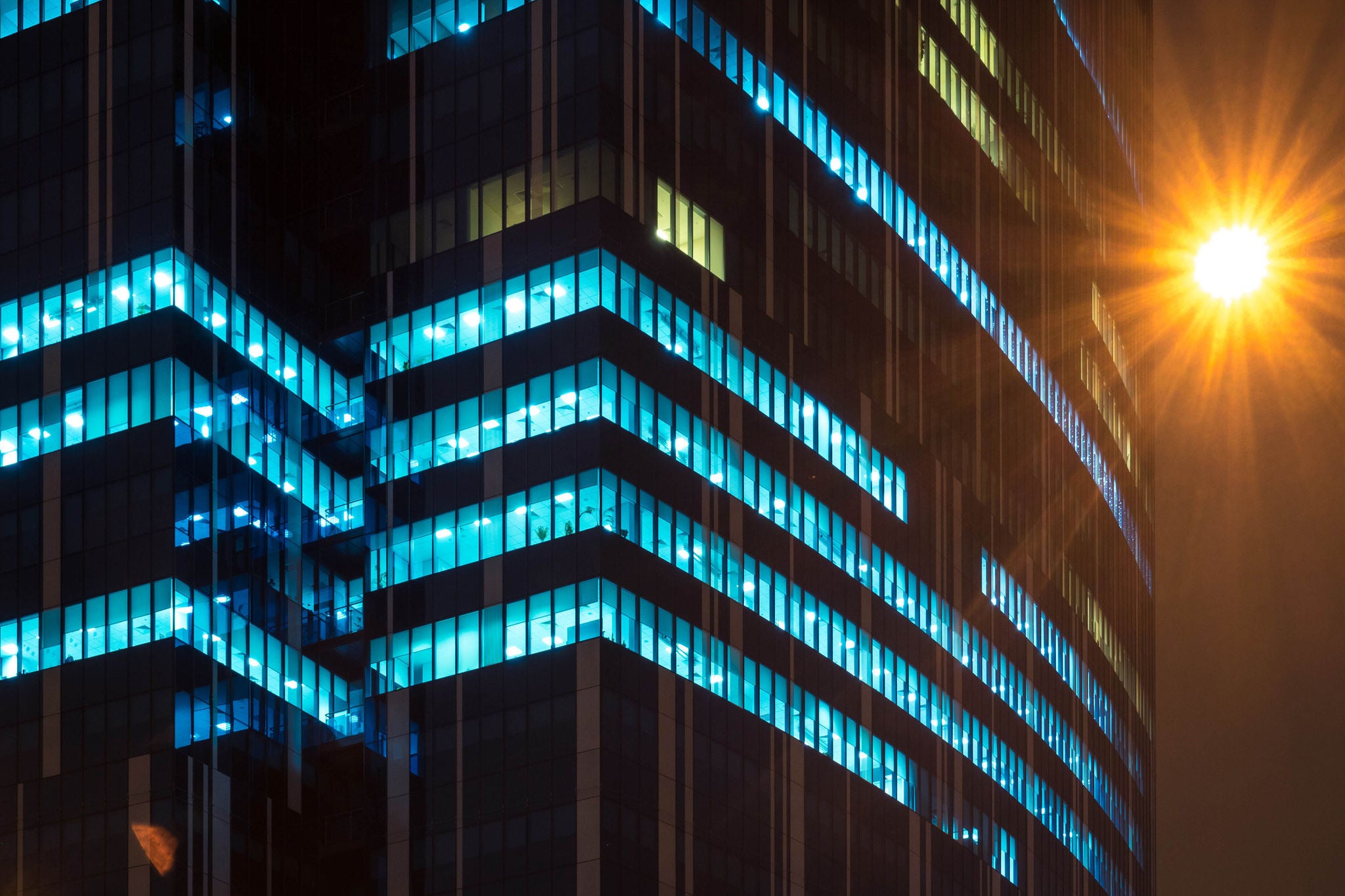Modern office windows of skyscraper glowing at night. Street light in the corner 