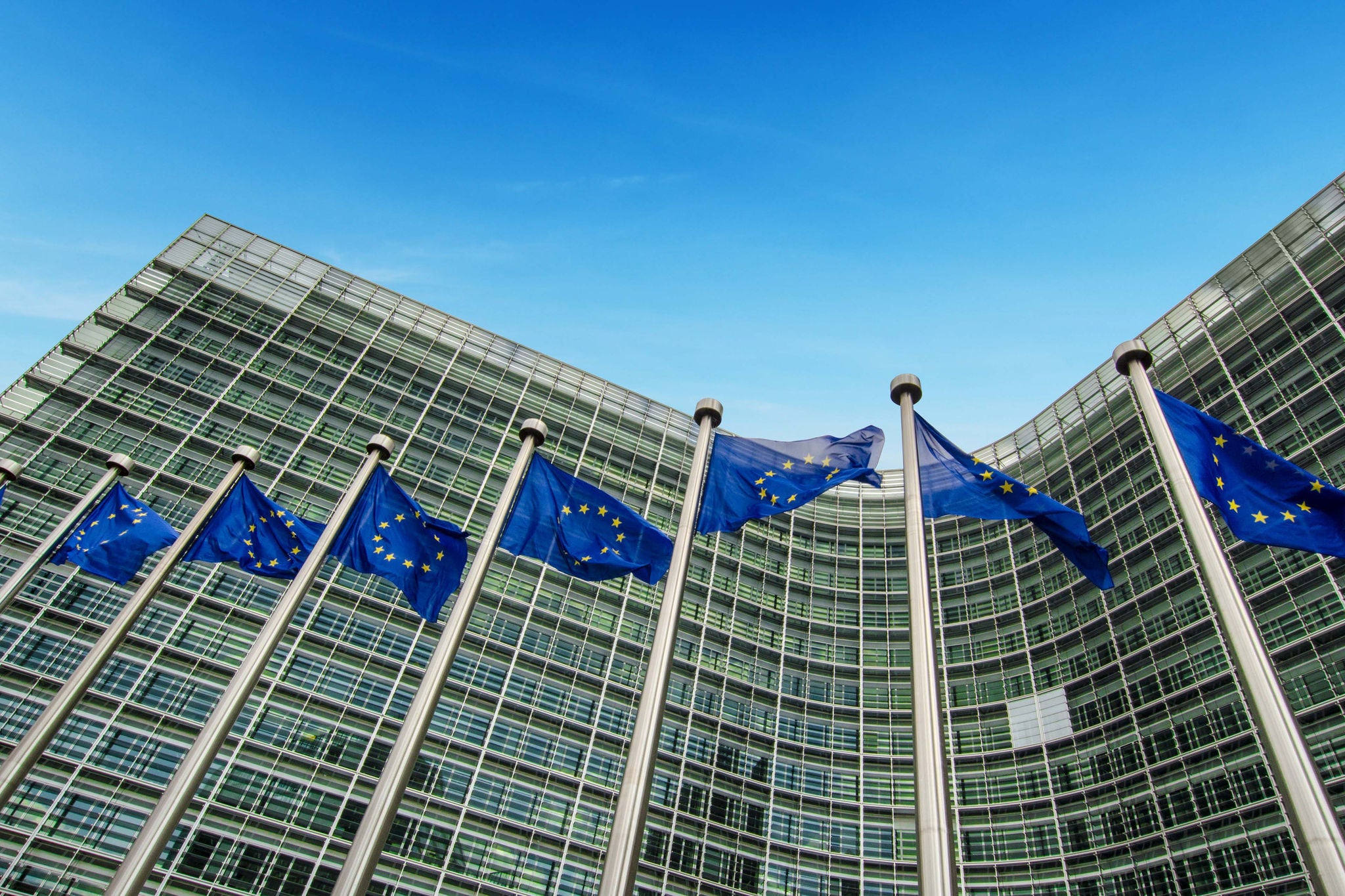 Mehrere EU-Flaggen vor moderner Glasfassade der EU-Kommission in Brüssel.