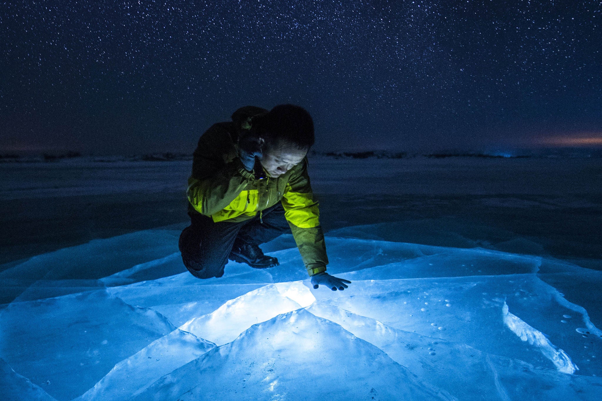Man shining torch throught the ice of a frozen lake