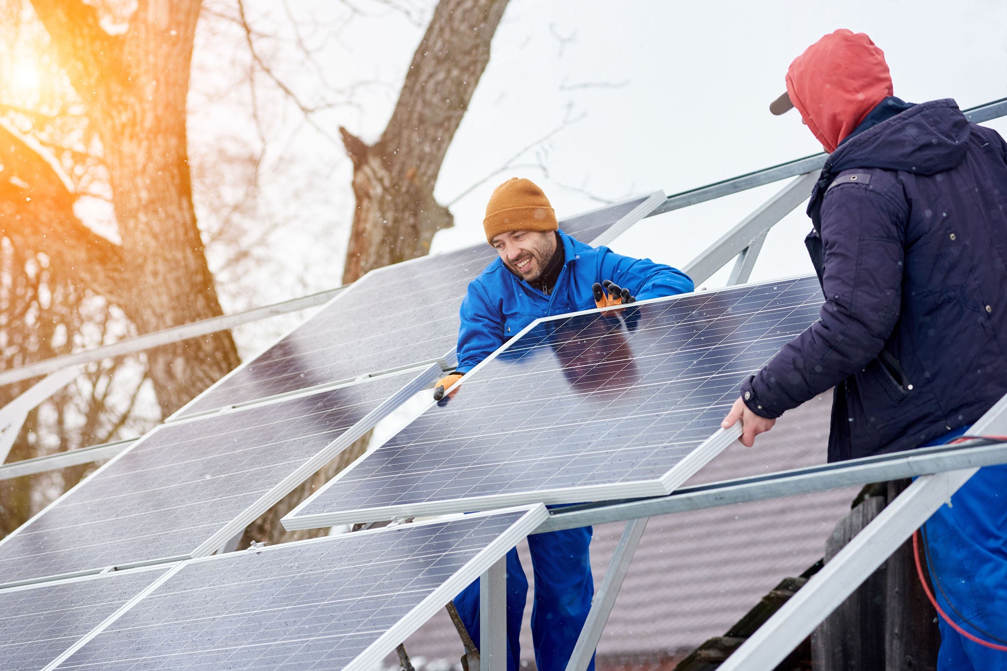 Technicians shown mounting blue solar panels on a roof on a snowy day