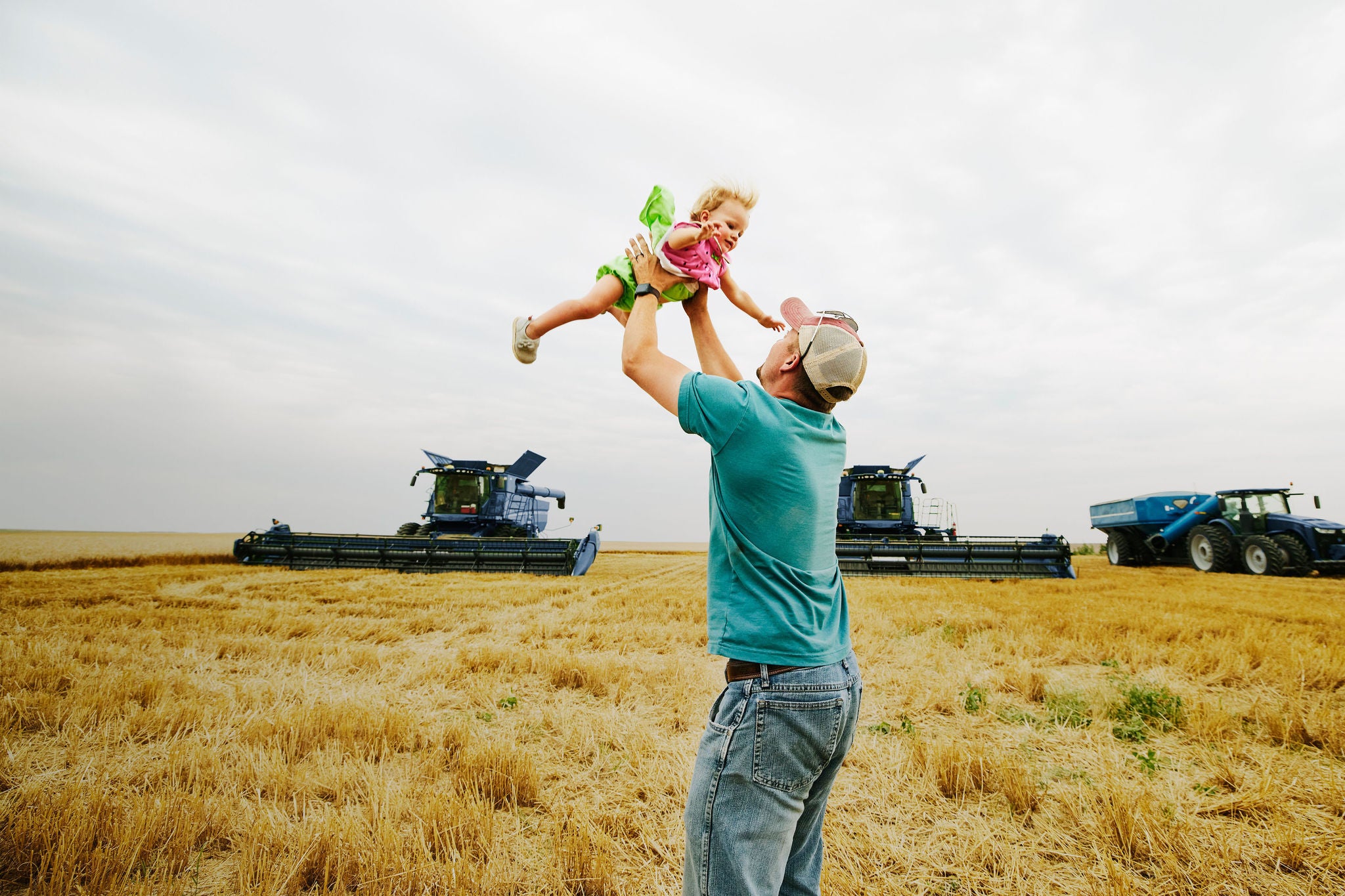 A farmer throwing young daughter up in air in wheat field during summer harvest