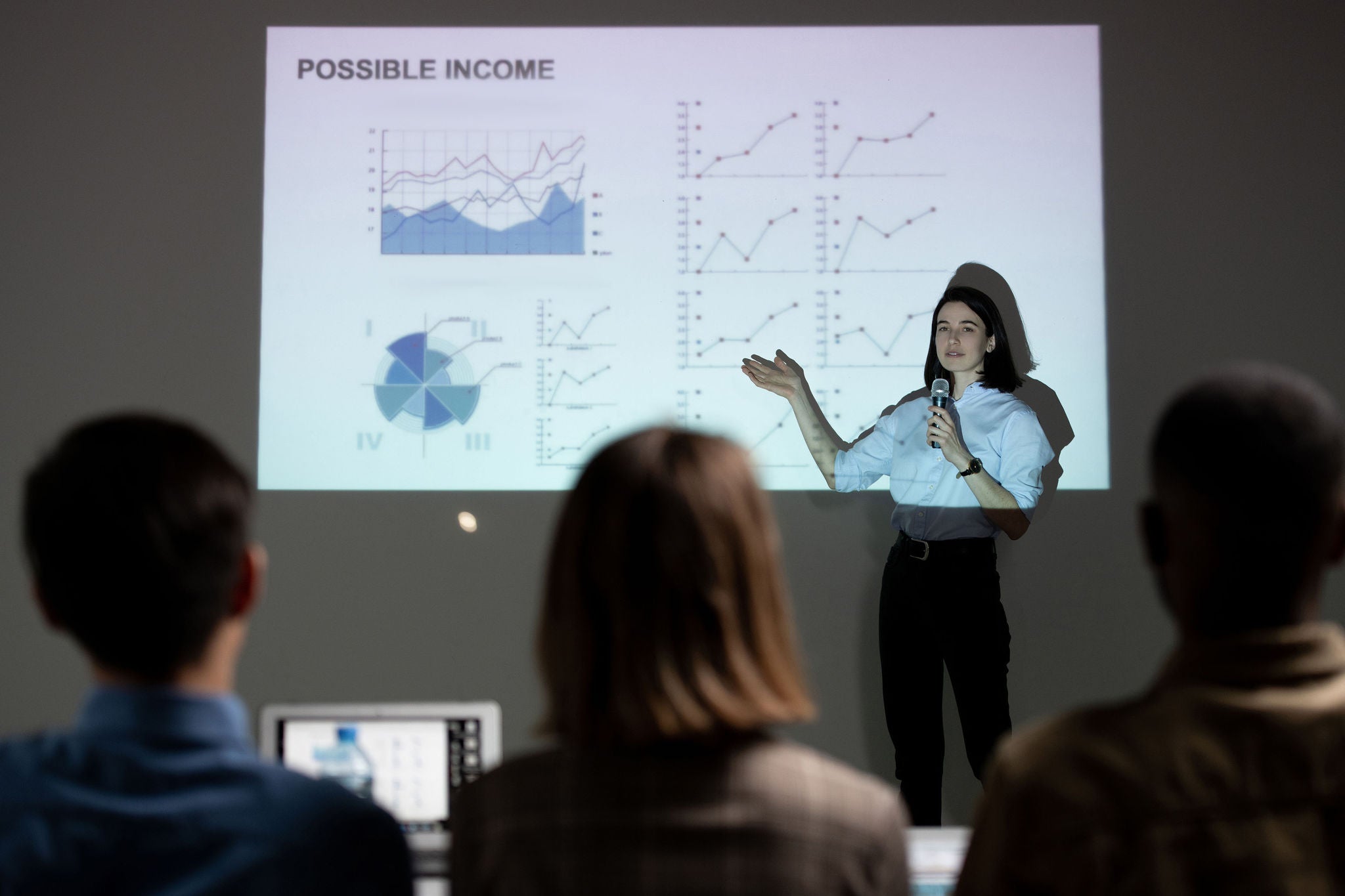 Young woman pointing at projection screen with graph variations and giving speech on own startup project in front of investors