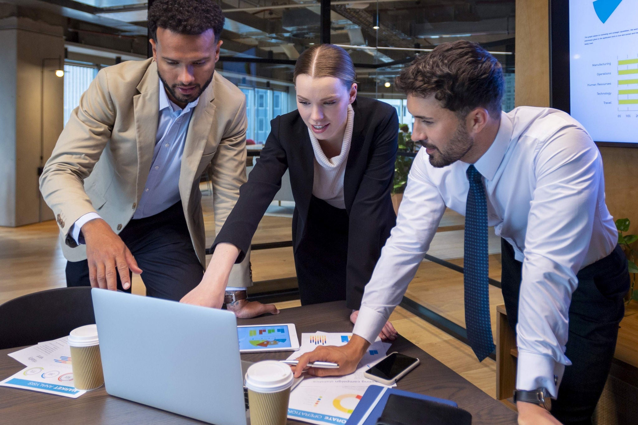 Three business professionals engage in a discussion while standing in a meeting room
