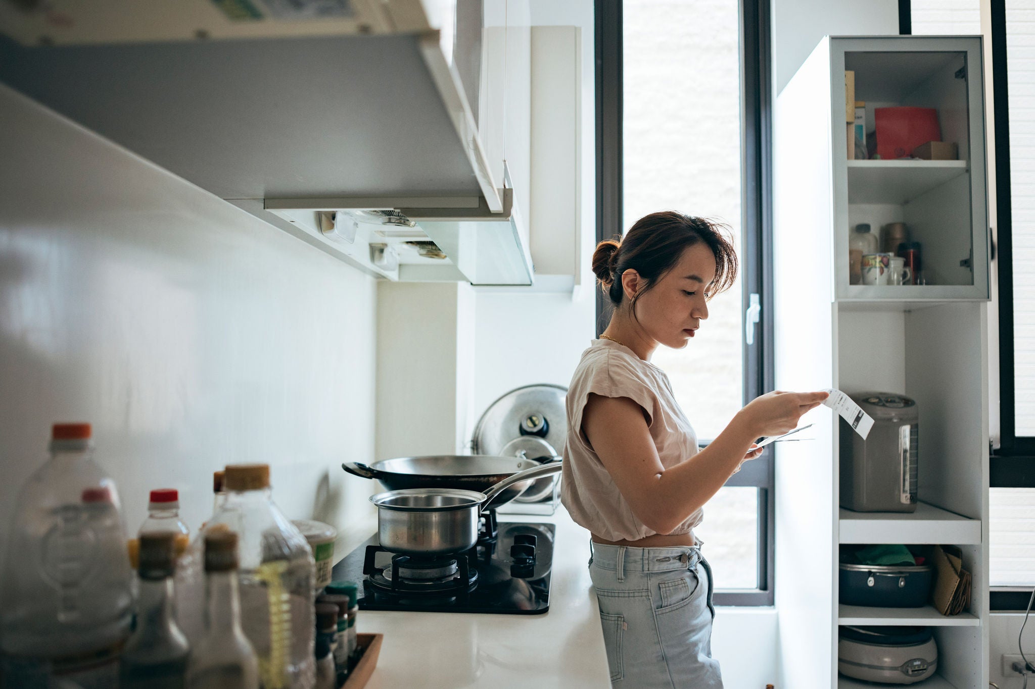 Individual reading a product label while standing in a bright, modern home kitchen.