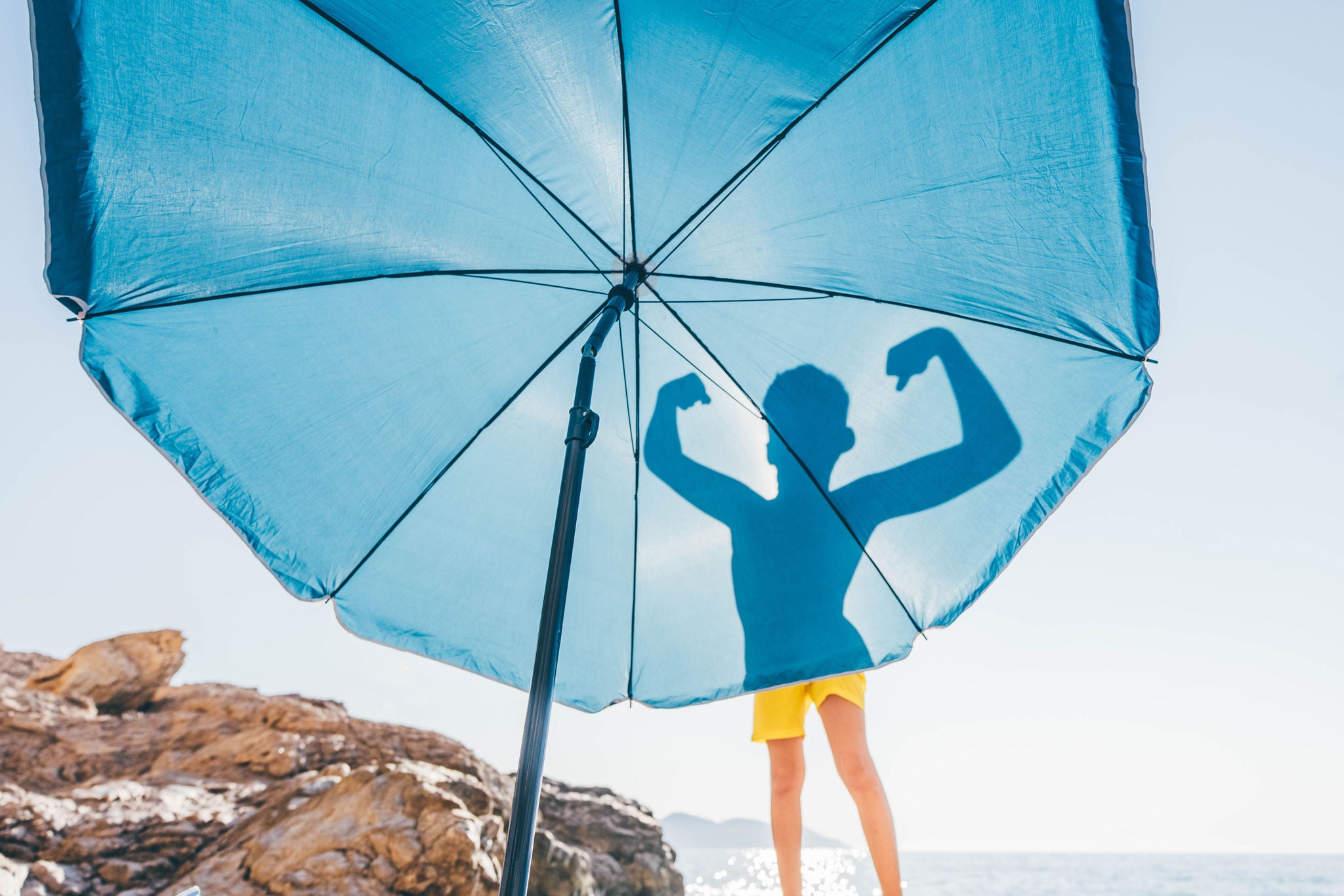 Silhouette of boy flexing his muscles on blue beach umbrella