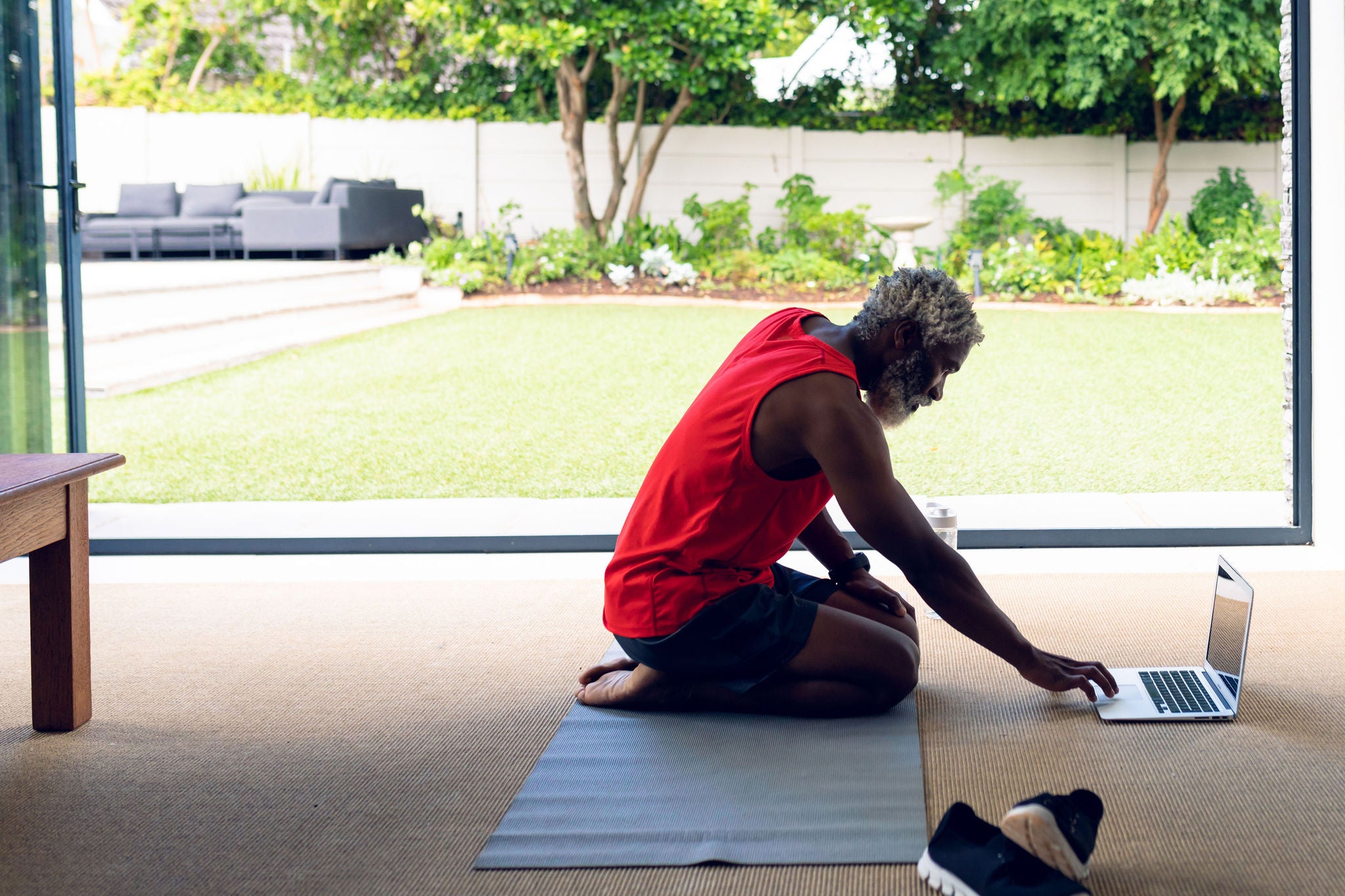 African american man using laptop while kneeling on yoga mat