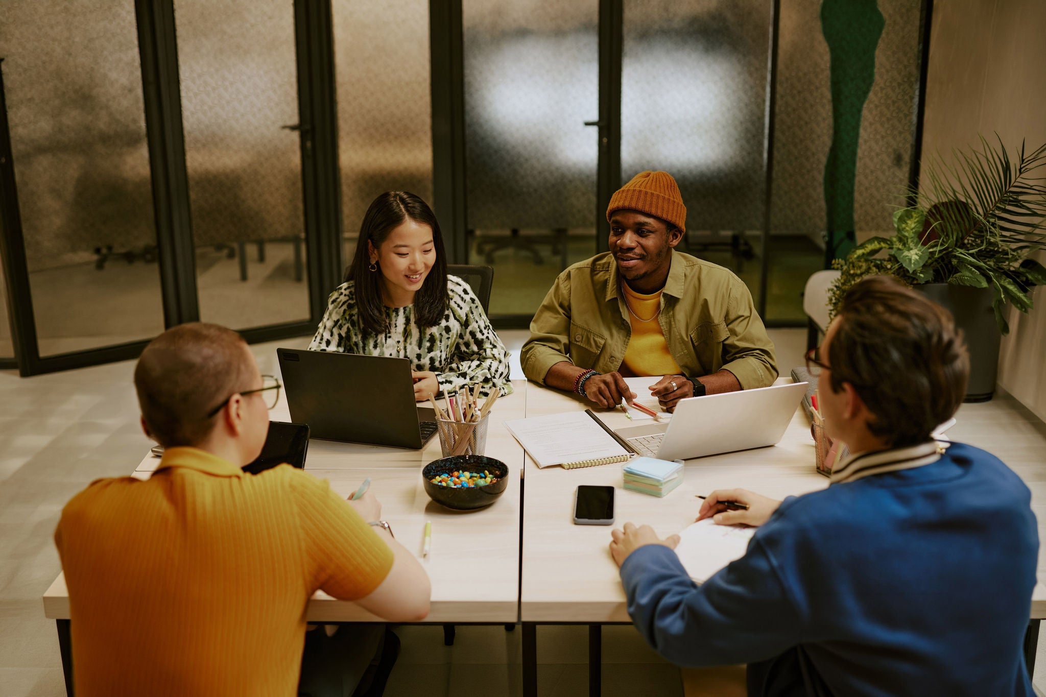 High angle view of multi-ethnic group of young colleagues sitting at table with laptops, gadgets and documents on top, discussing work plan
