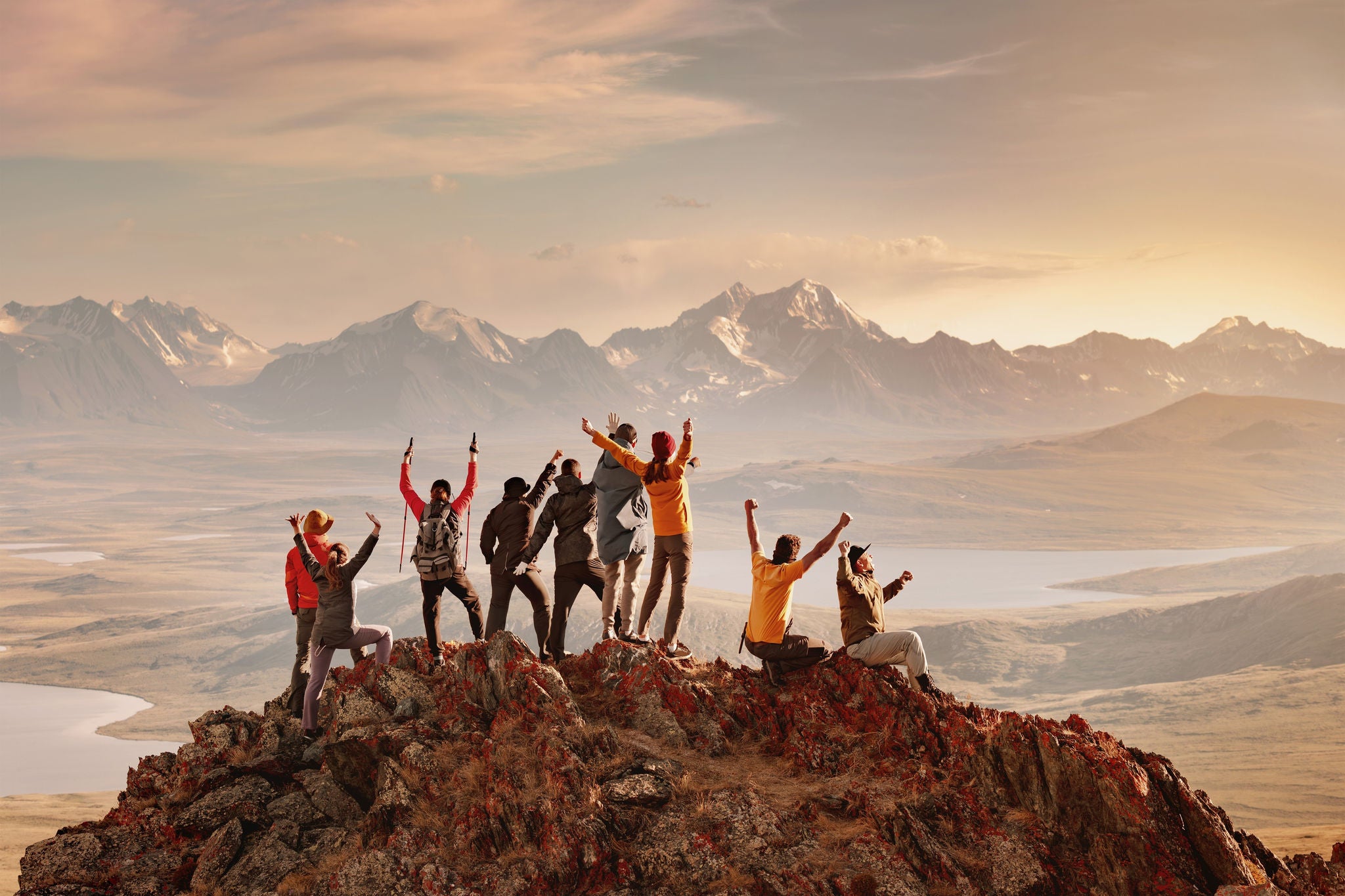 Wandergruppe jubelt auf Berggipfel bei Sonnenuntergang, Symbol für Teamarbeit und Erfolg
