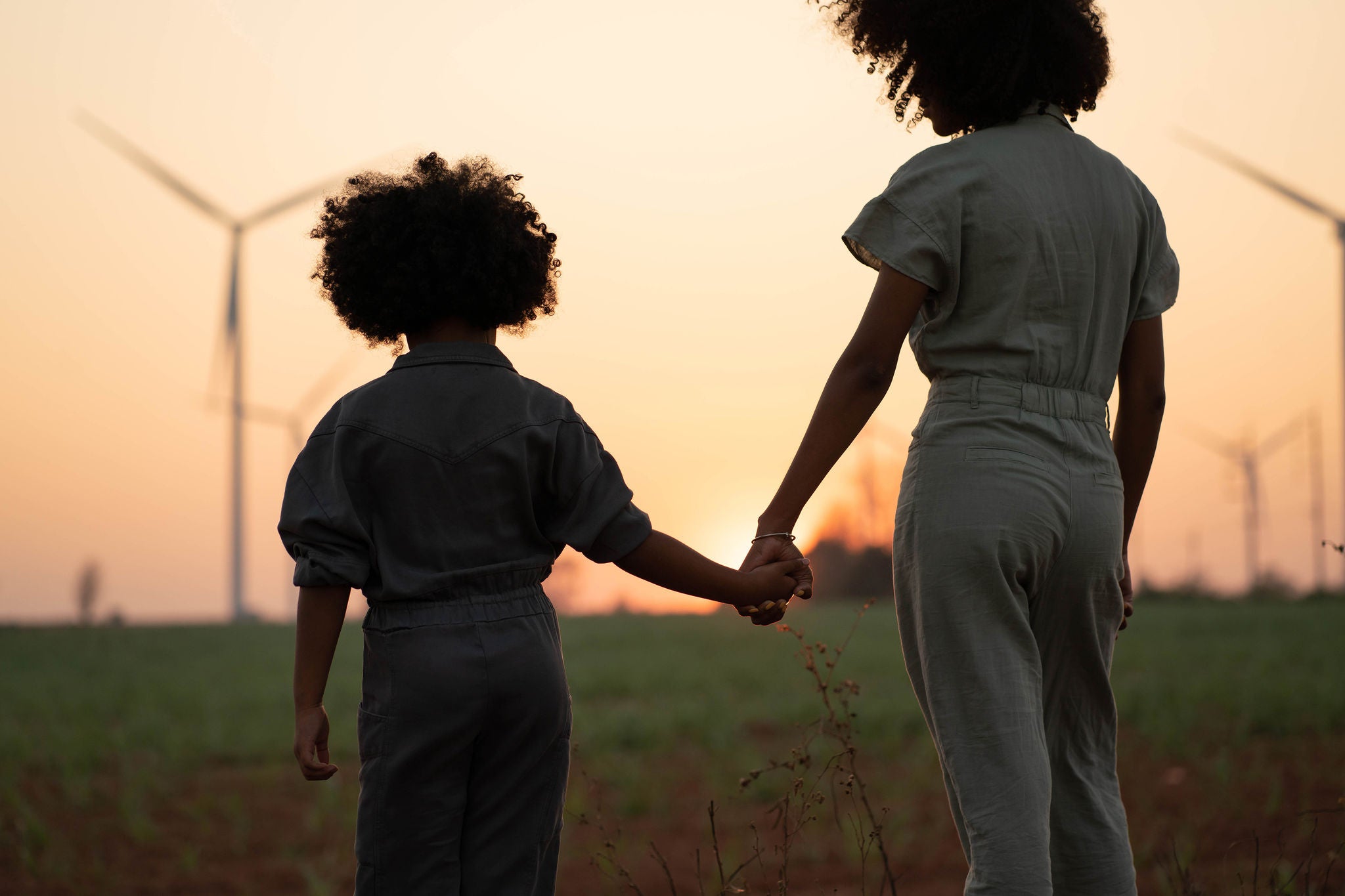 Mother holding her child's hand as they look at wind turbines in the distance.