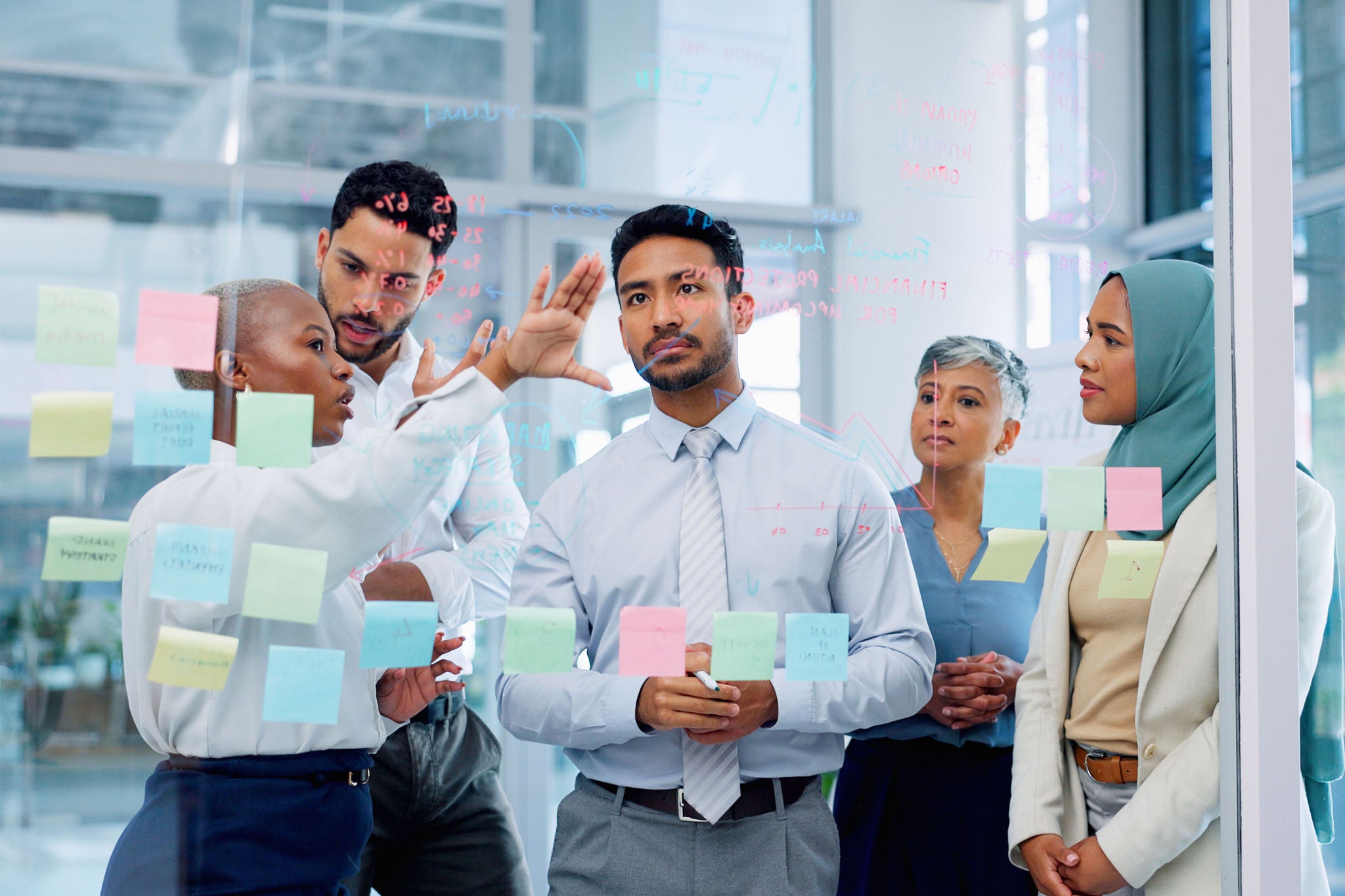 business man training a team while planning strategy on glass in an office. Teamwork, diversity and workshop with a man and woman employee group at work
