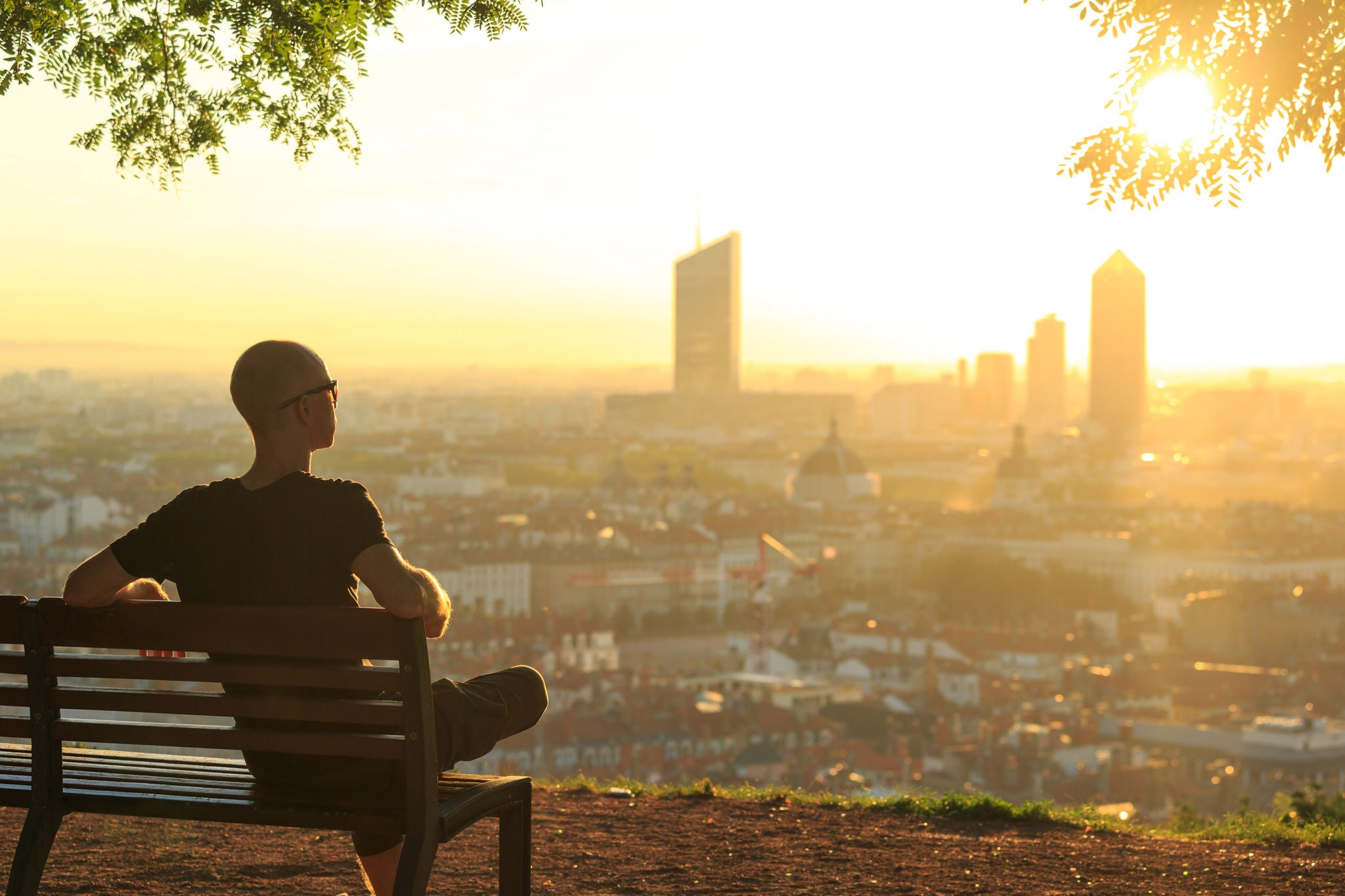 Man on park bench enjoying summer sunrise over a city in France
