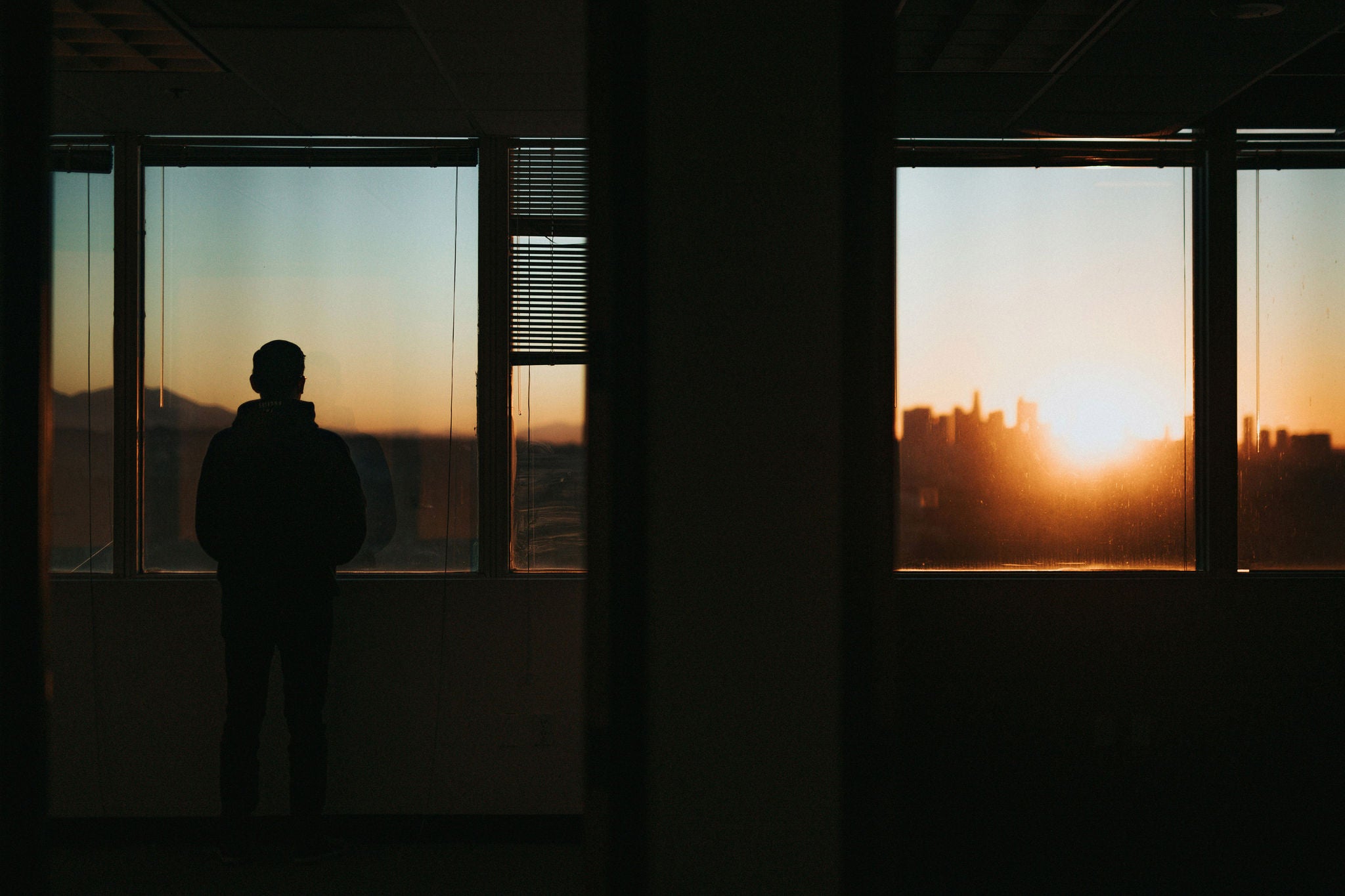 Silhouette of a person standing near large windows looking out at a city skyline