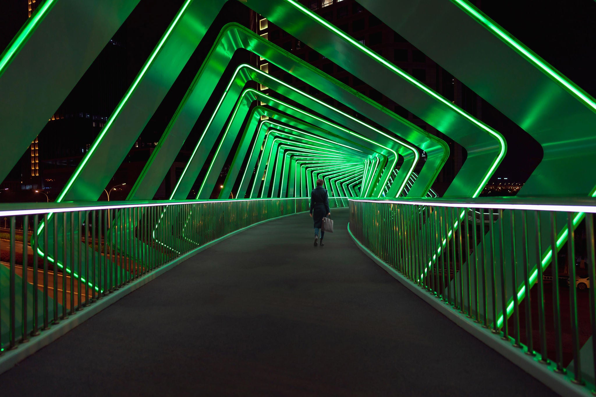 Mujer cruza un puente peatonal con luces verdes