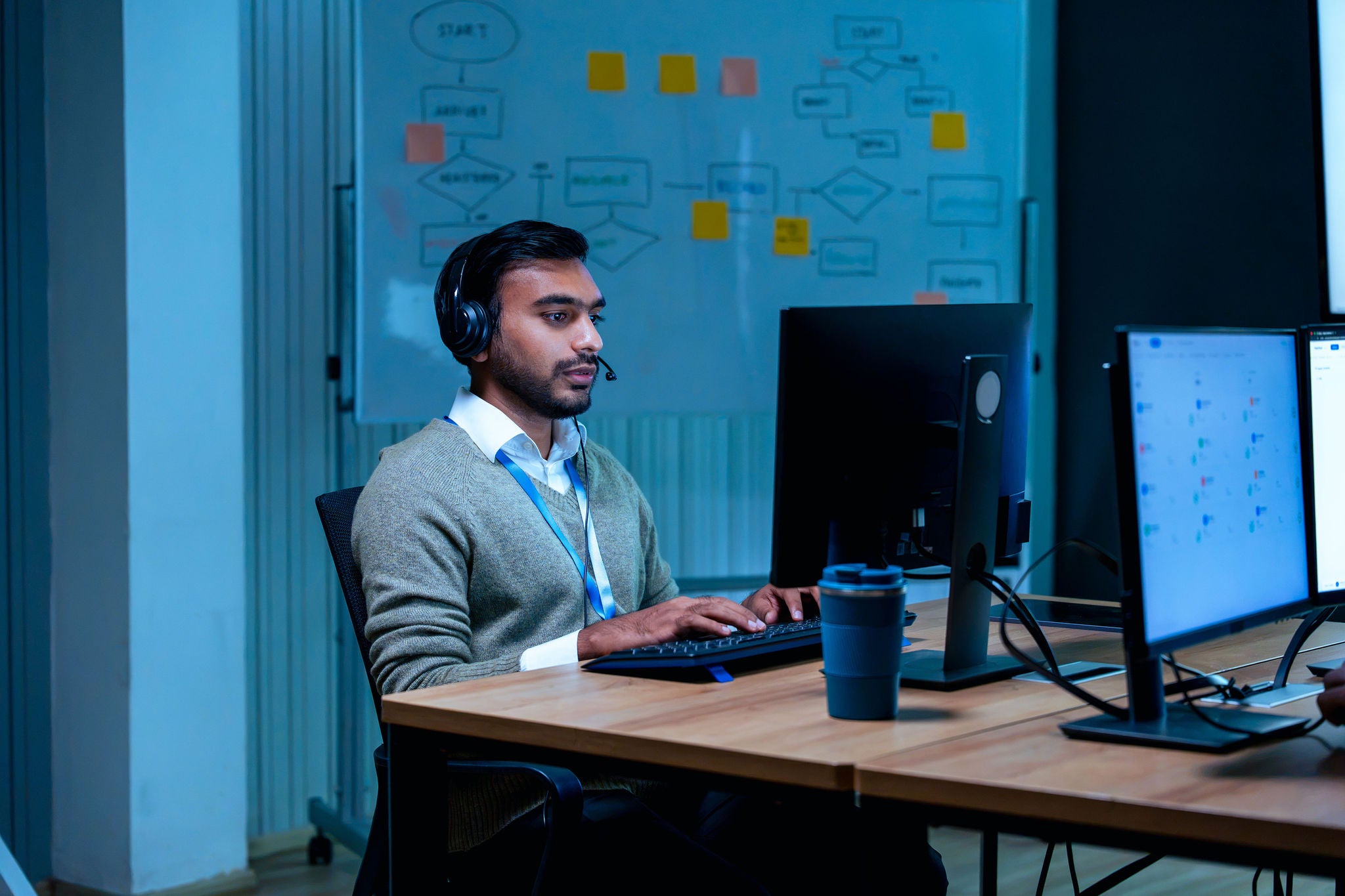 Indian customer support agent wearing headset working on computer late at night in modern dark office setting