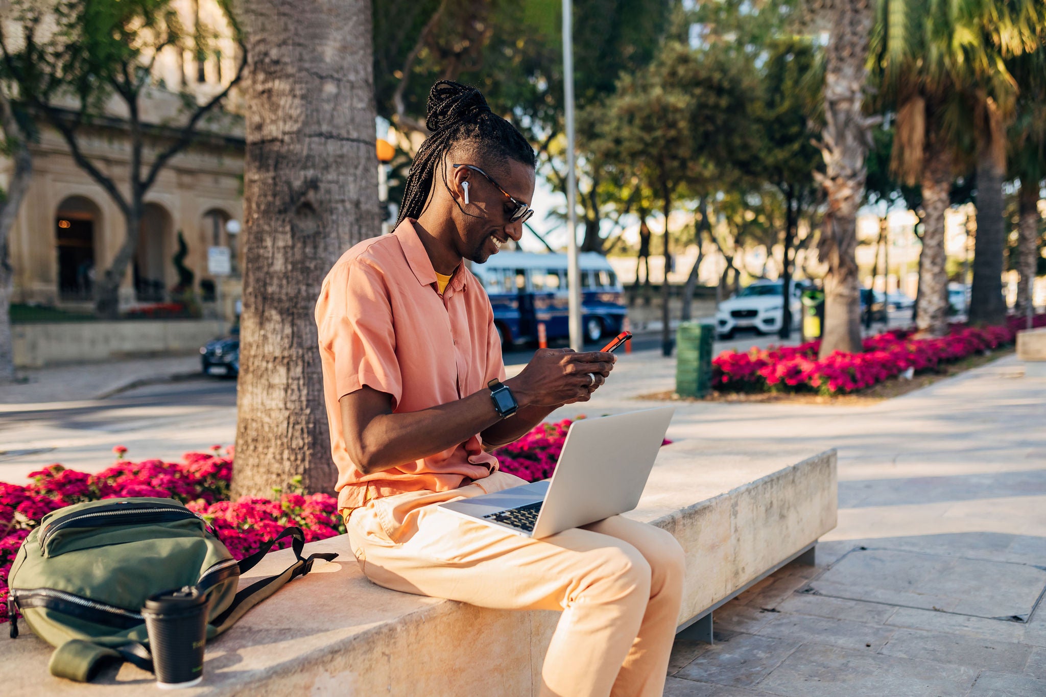 Business man dressed in casual clothes working on laptop and  using mobile phone while sitting in the park on a sunny day