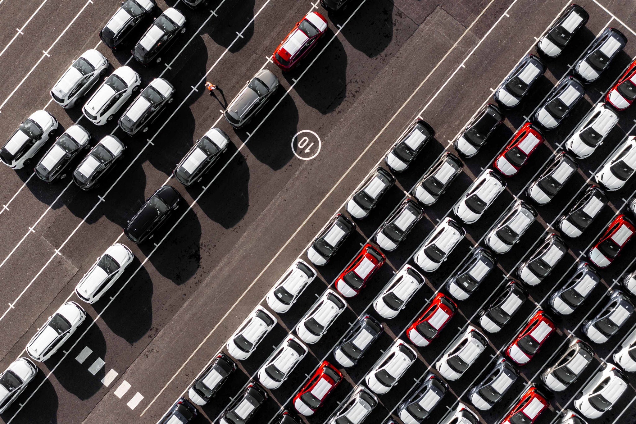 An aerial view directly above rows of newly built cars in the automobile industry on a commercial dock ready to be loaded and shipped for export and import with American vehicle tariffs