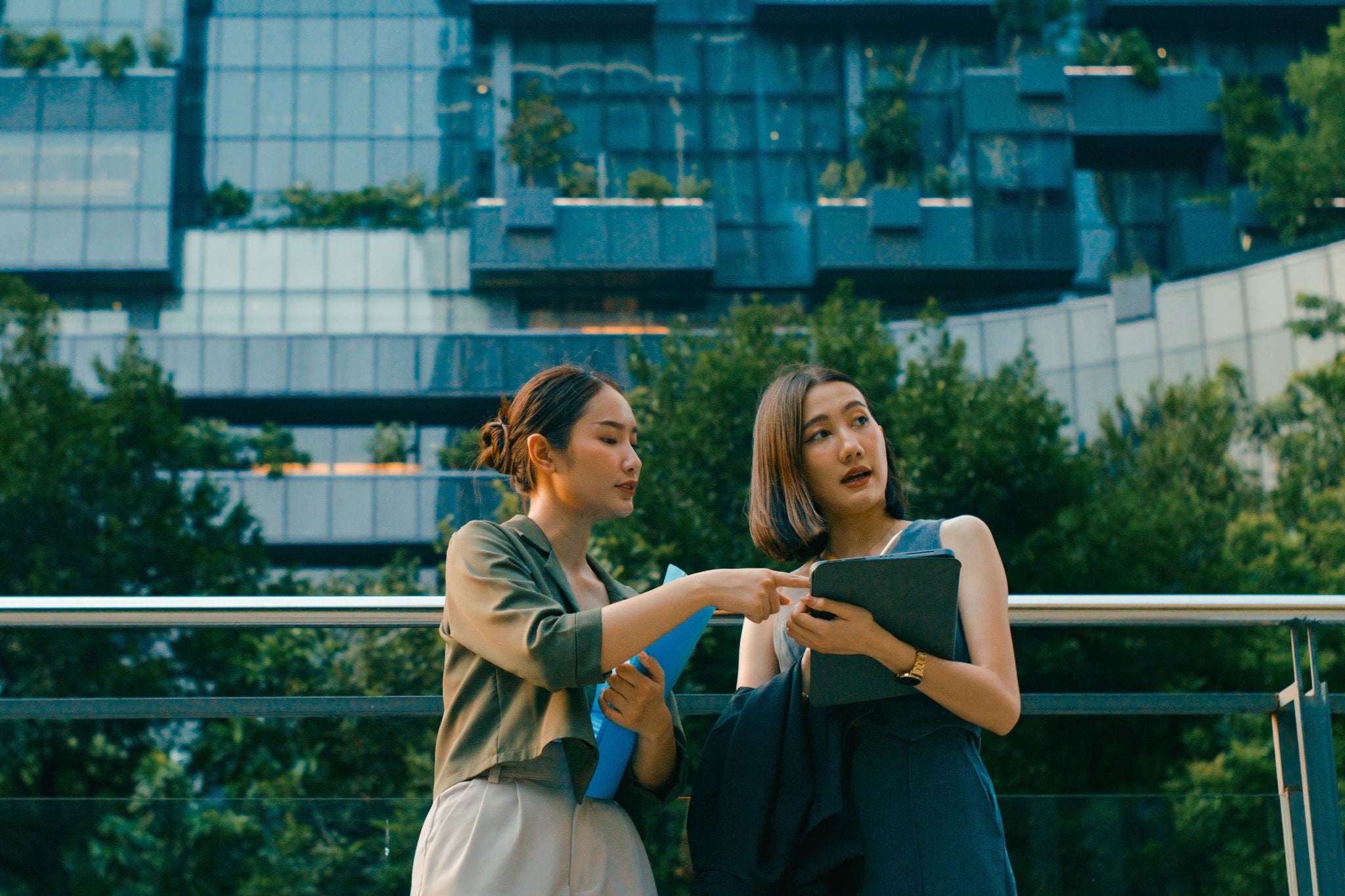 Two young Asian businesswomen meeting business strategy discussion talk outside modern office building. Sustainable business outdoor concept.