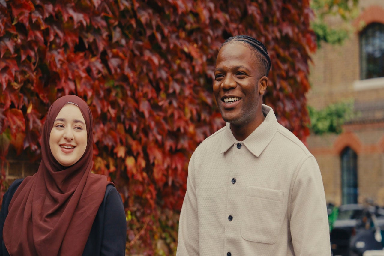 Two people outdoors by red ivy wall