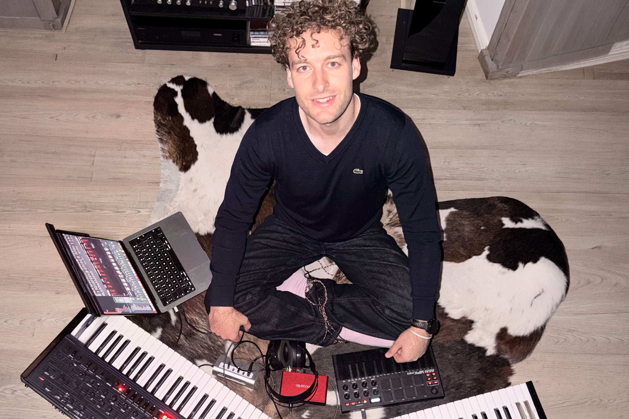 Junger Mann sitzt mit Musik-Instrumenten auf dem Boden eines Zimmers