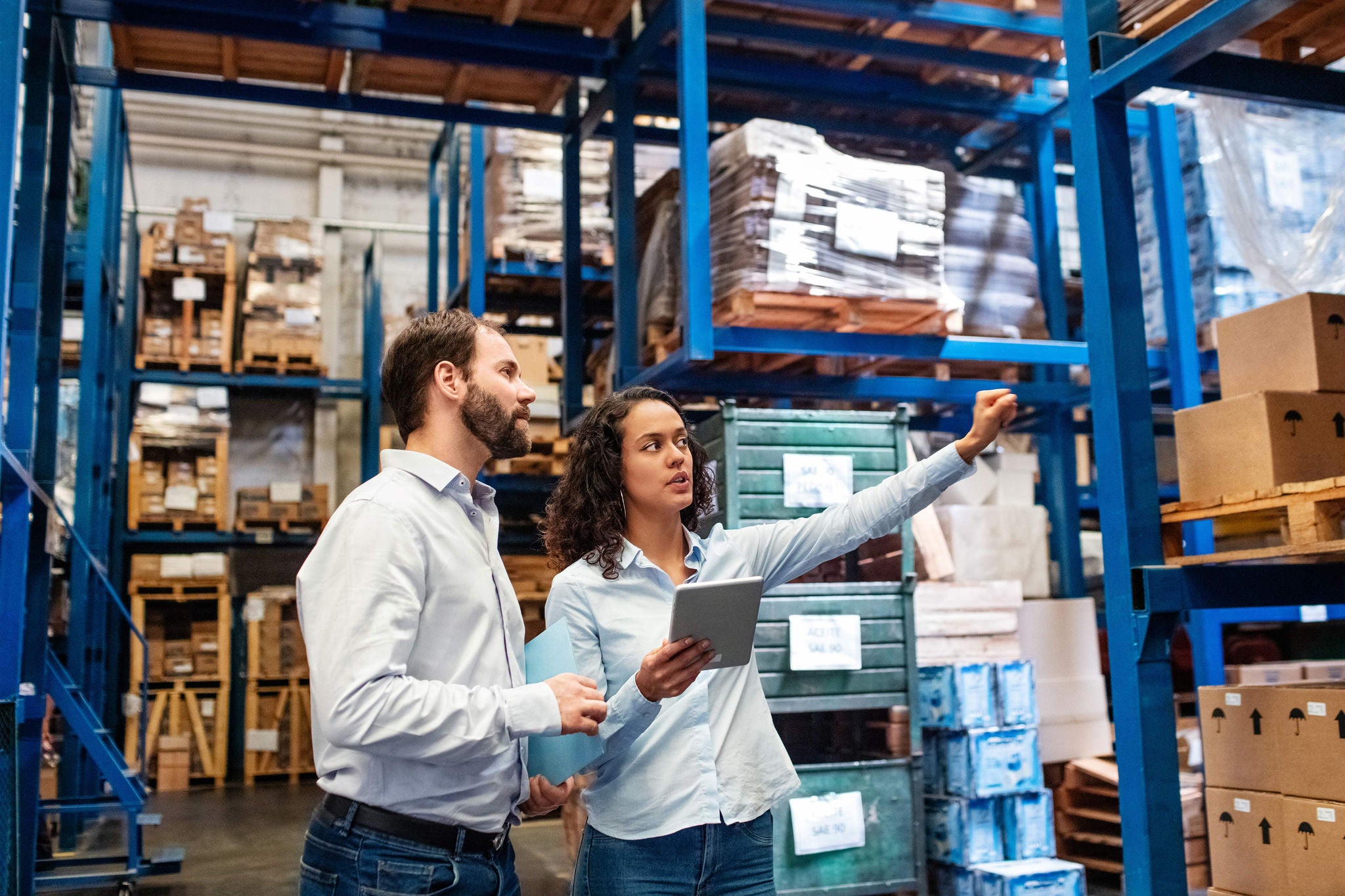 Businesswoman with a digital tablet showing and talking with male worker in distribution warehouse. Manager working with foreman in warehouse checking stock levels.