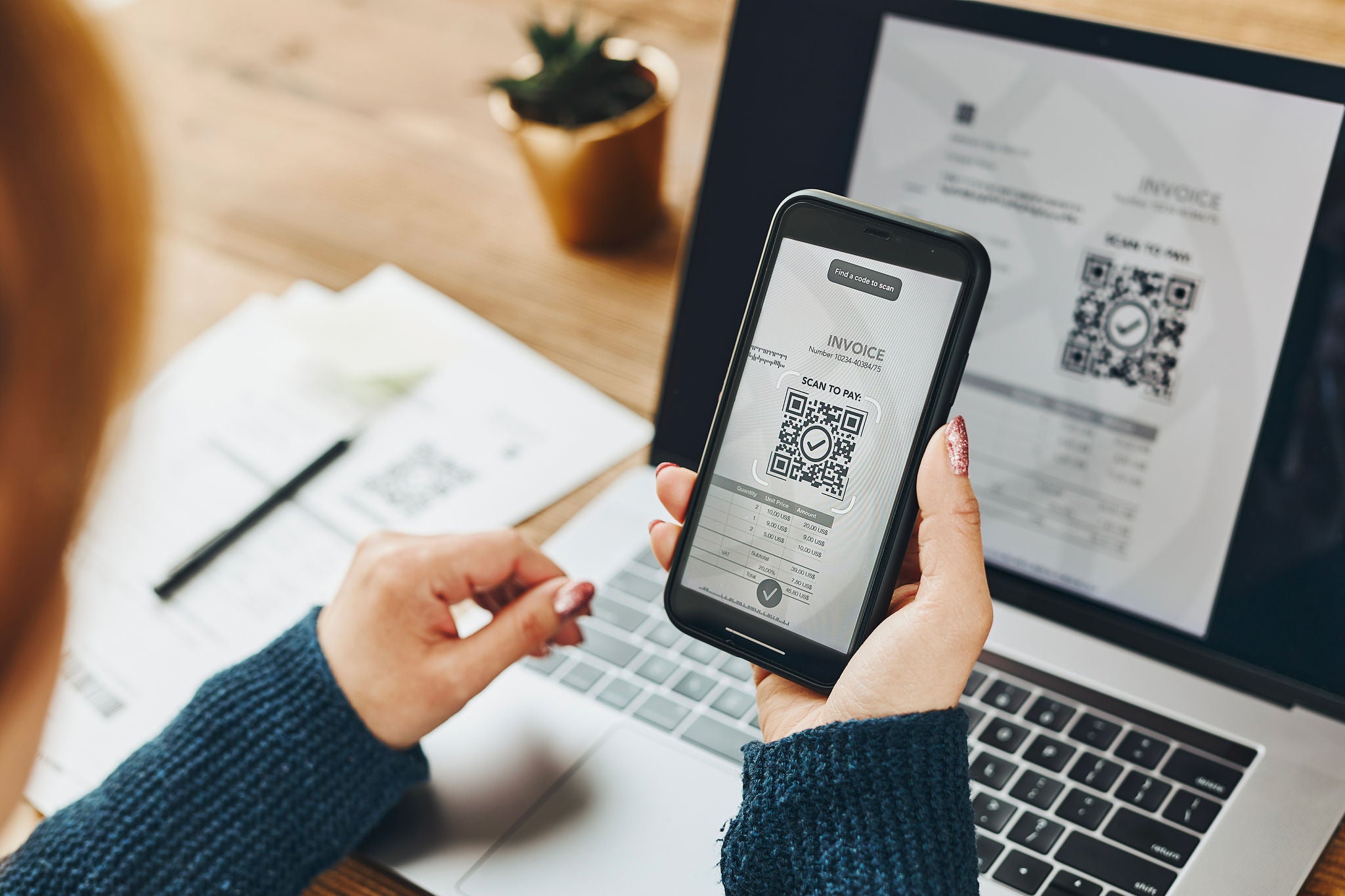 Woman scanning QR code from invoice to make payment using fast secure payment system and smartphone code reader. Business woman paying bills using express payment technology. Paying expenses online