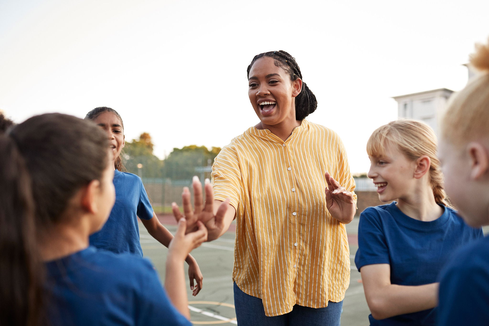 Happy coach enjoying with students in schoolyard at sports day