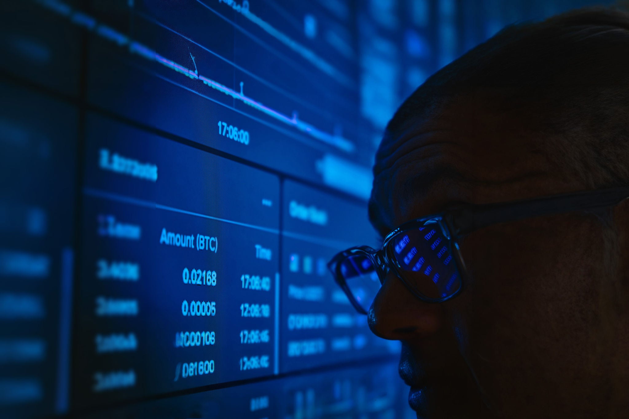 Man watching live cryptocurrency trading data on a blue lit computer monitor