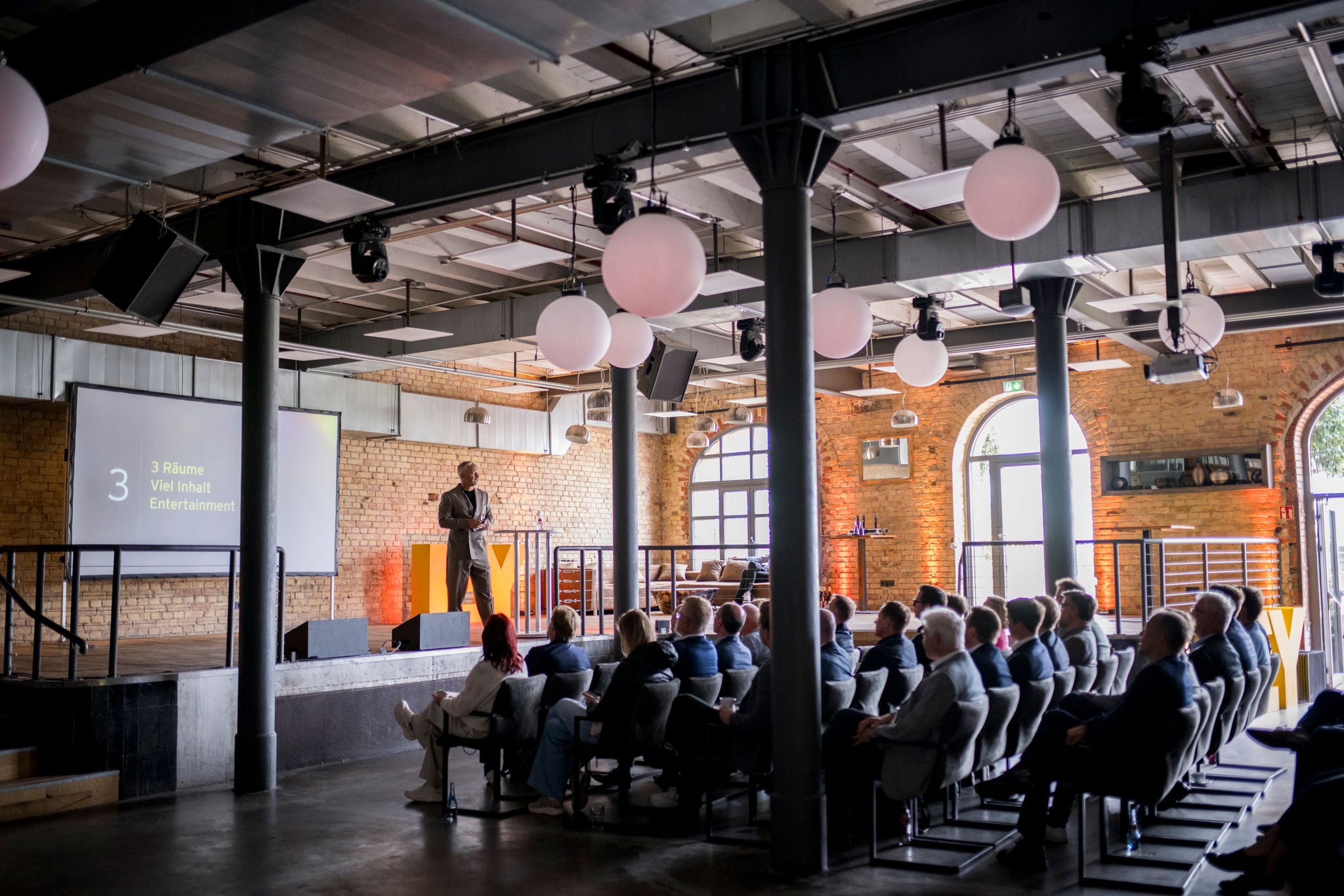 Publikum verfolgt Präsentation bei Business-Event in industriellem Raum