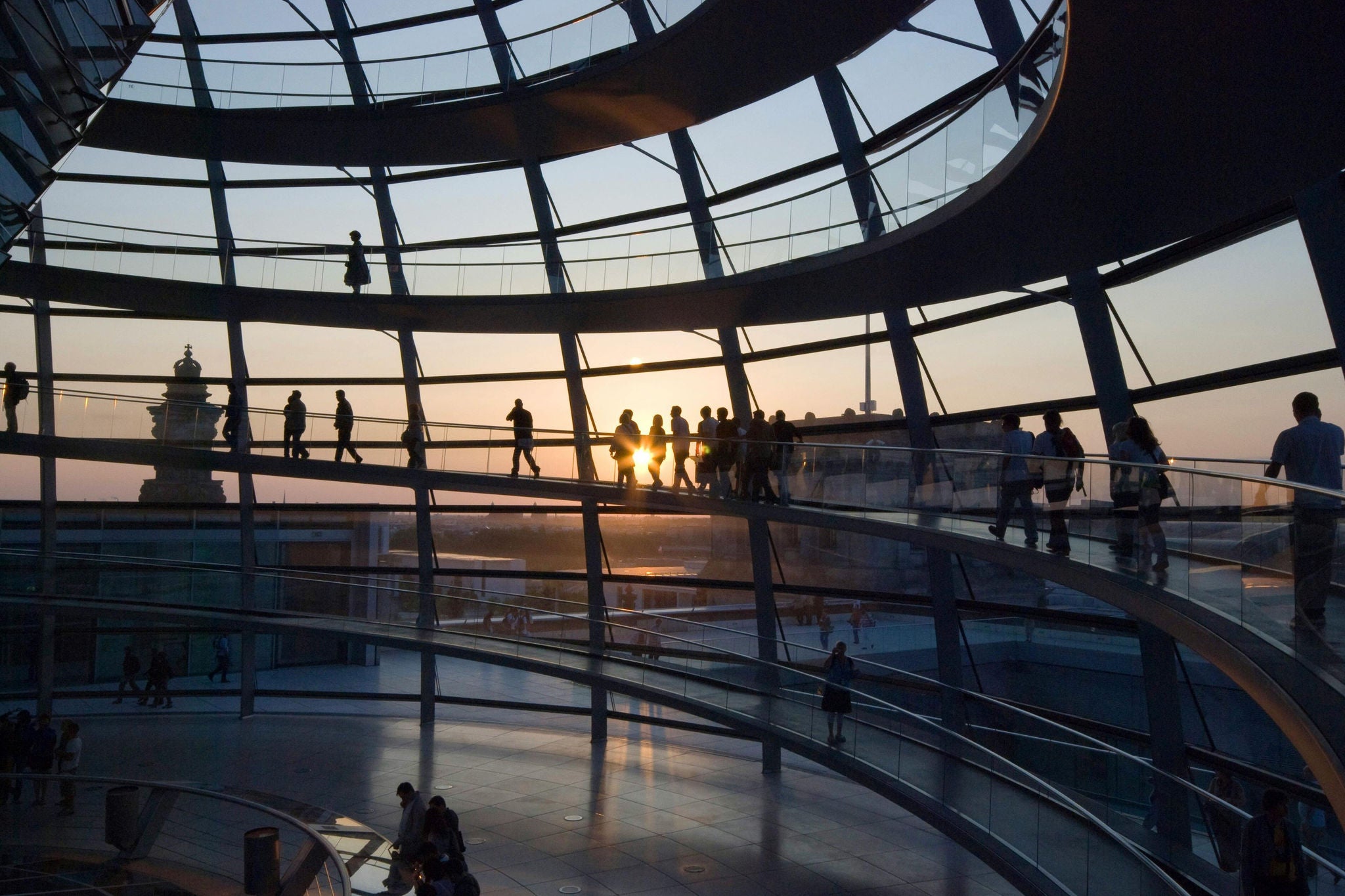 People walking inside a modern glass dome building with curved walkways at sunset