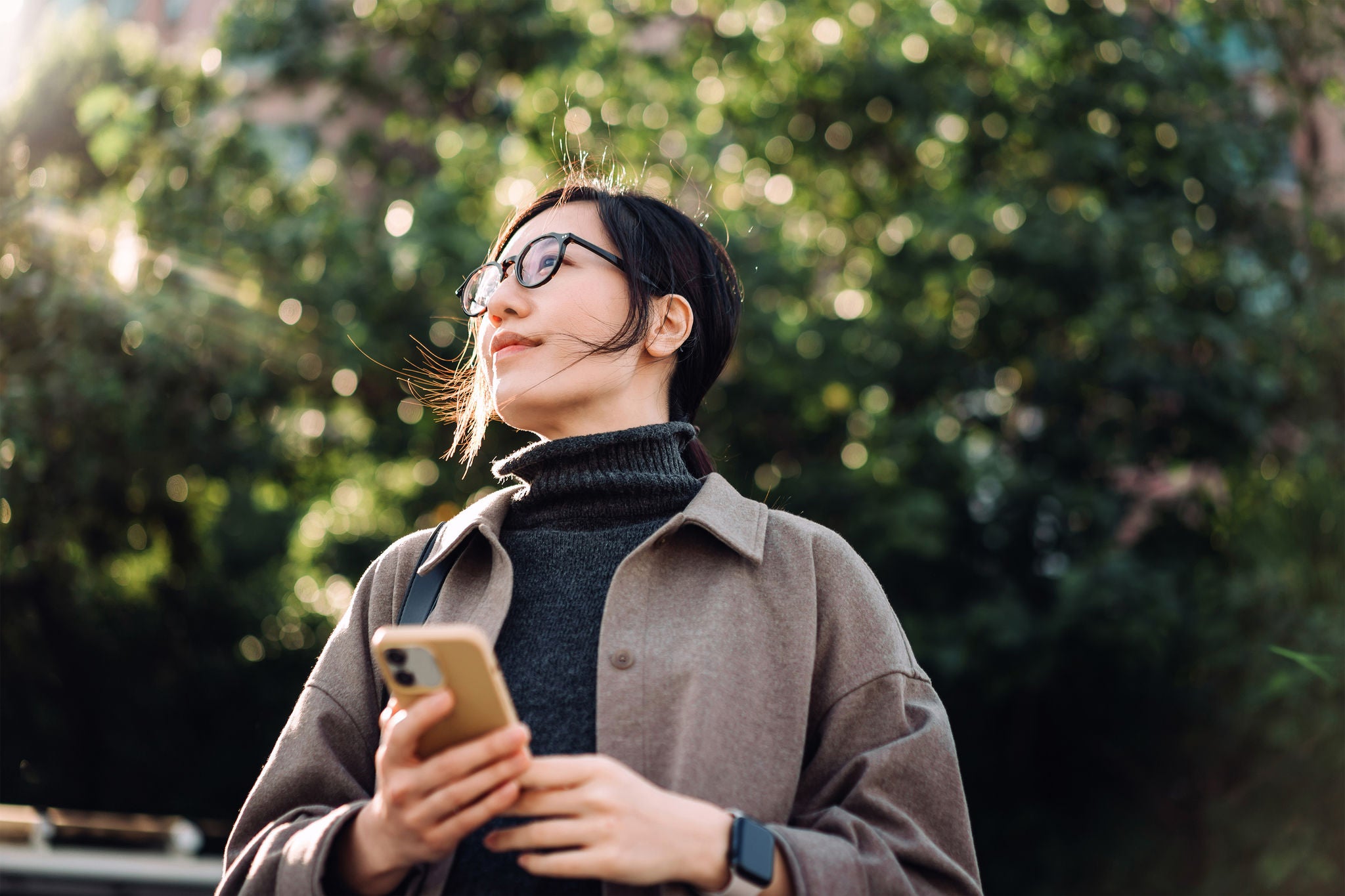 young Asian woman using smartphone in park against sunlight