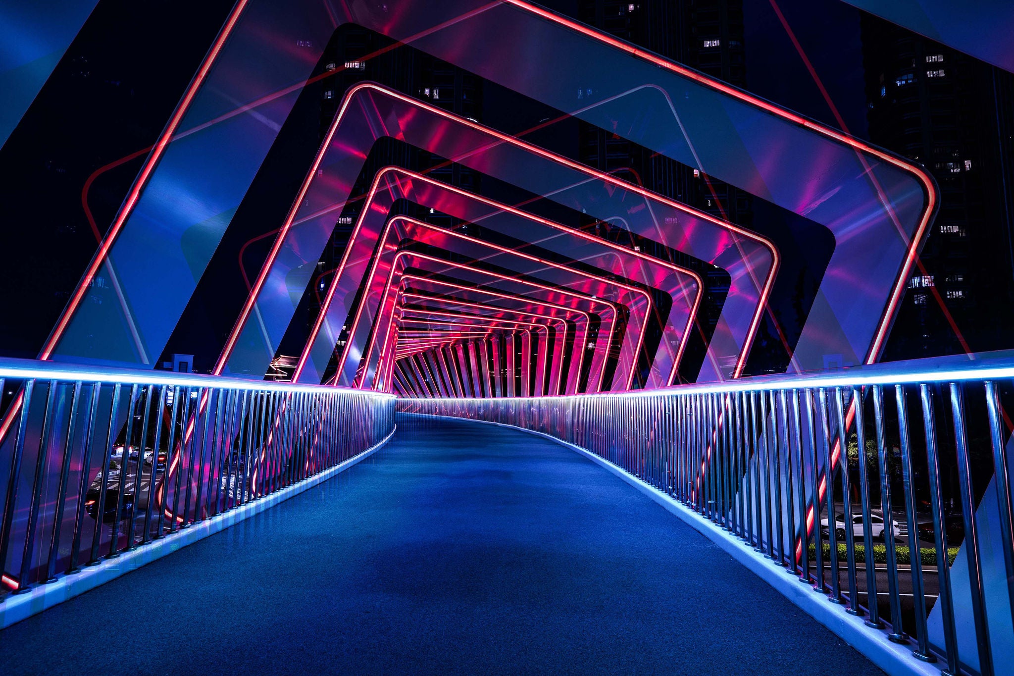 Beleuchtete Fußgängerbrücke mit geometrischen Neonrahmen in Blau und Pink, erzeugt einen modernen, dynamischen Effekt.