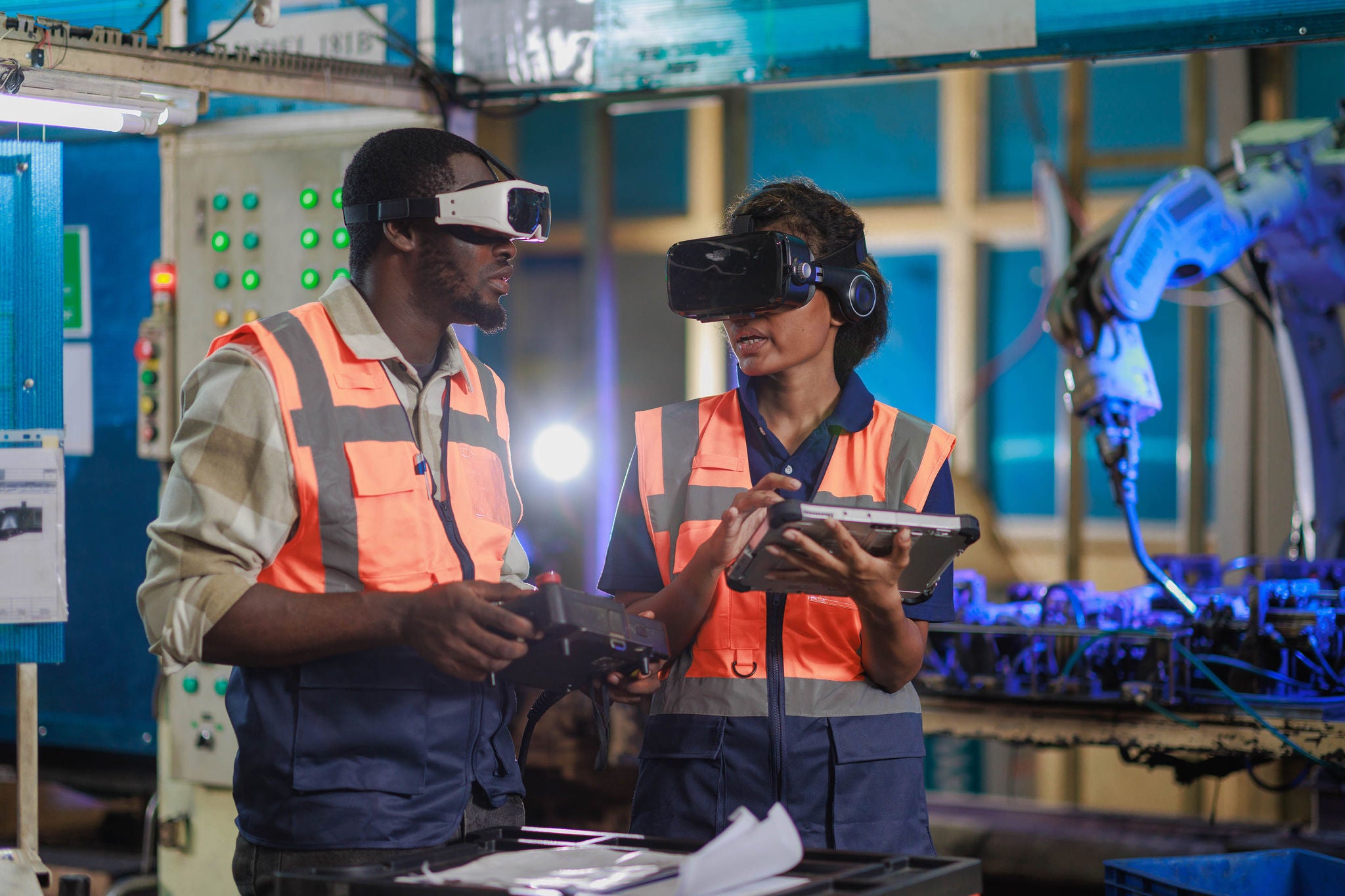 Two African engineers controlling the robotic welding arm in the factory production line using vr glasses.
