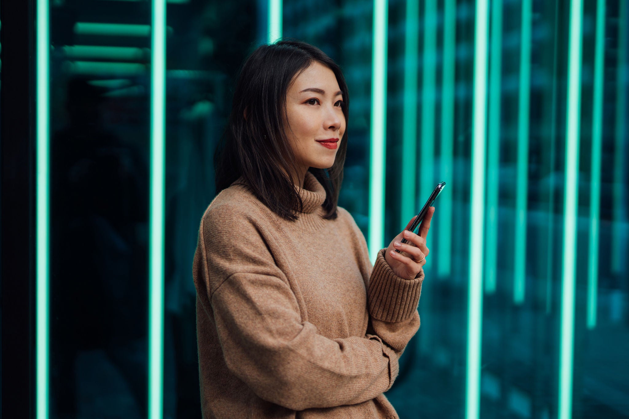 Junge Frau nutzt ihr Mobiltelefon vor einem futuristischen holografischen Hintergrund. Neue Investitionsmöglichkeiten – Aktien und Kryptowährungen über eine mobile App kaufen.