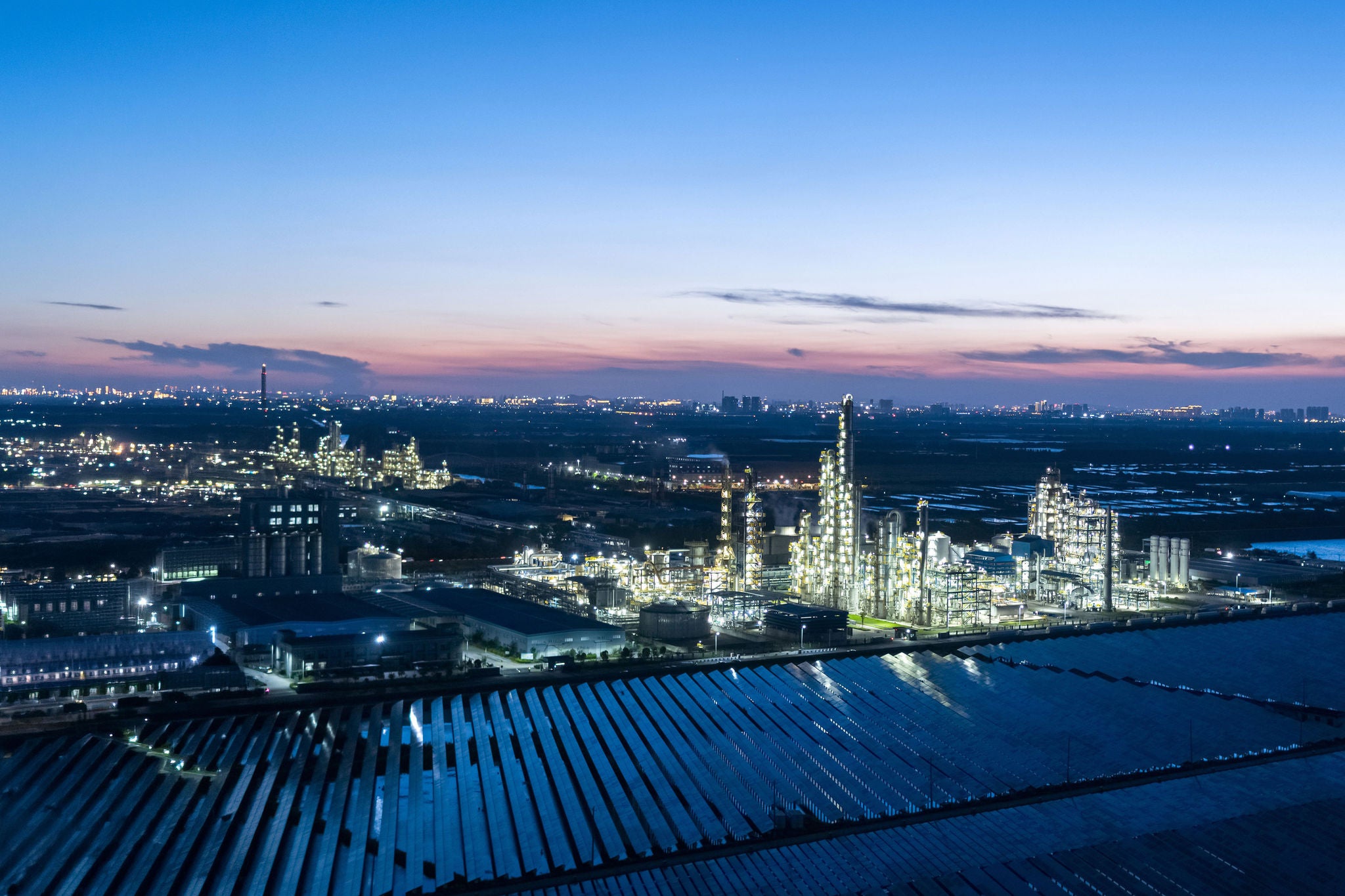 Beleuchtete Chemieanlage mit Solarmodulen bei Nacht