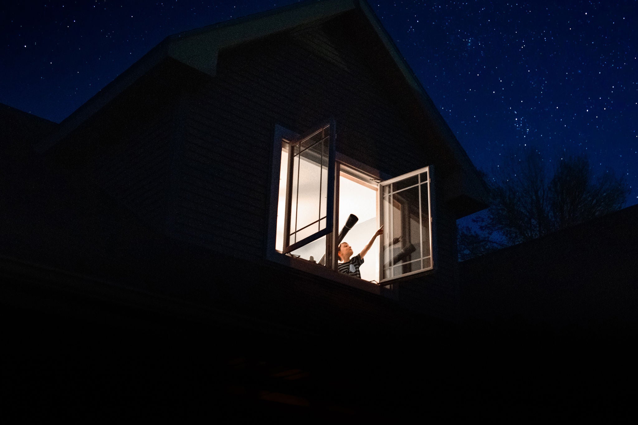 a child pointing to the stars from his bedroom window