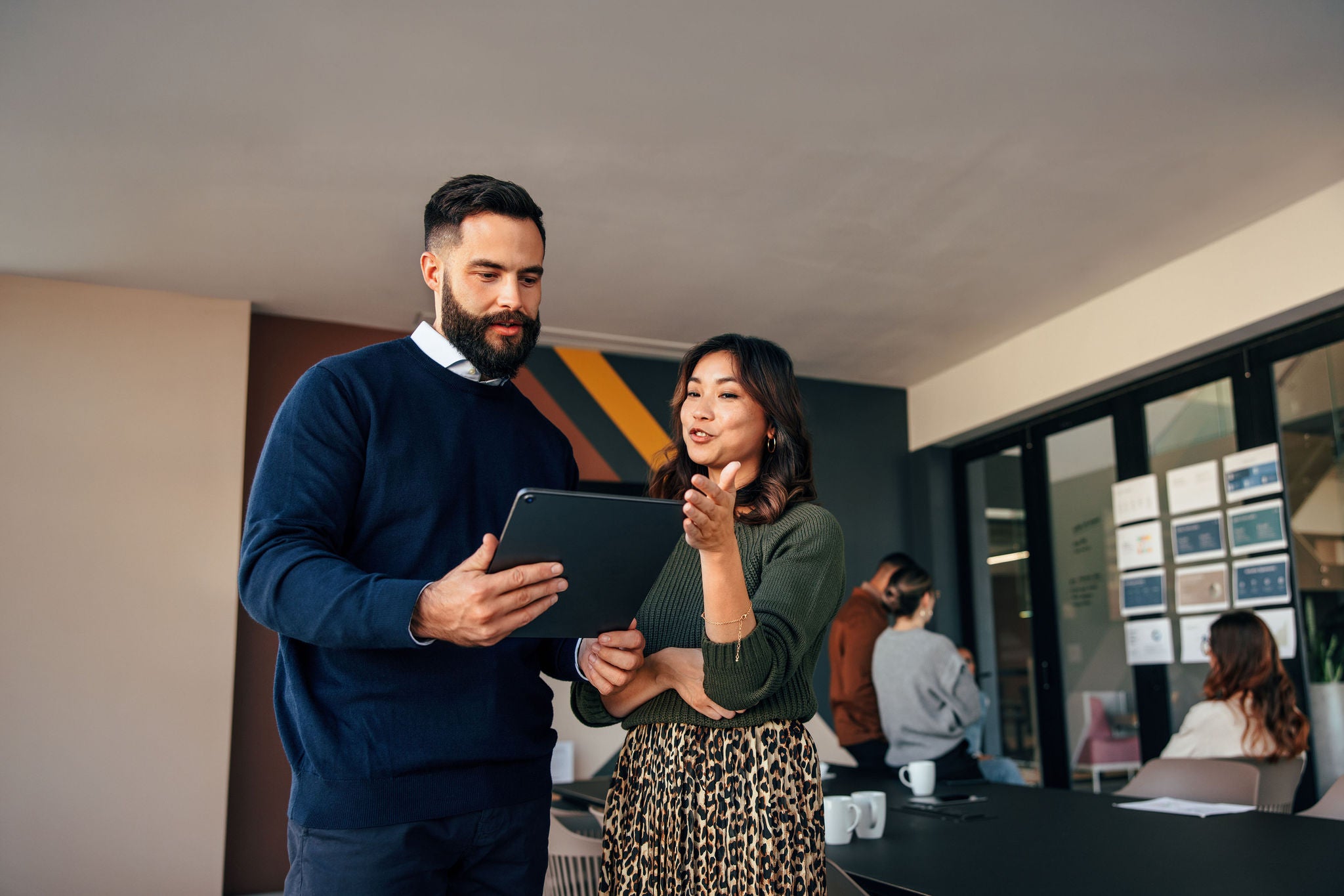 Two young businesspeople using a digital tablet while standing in a boardroom.