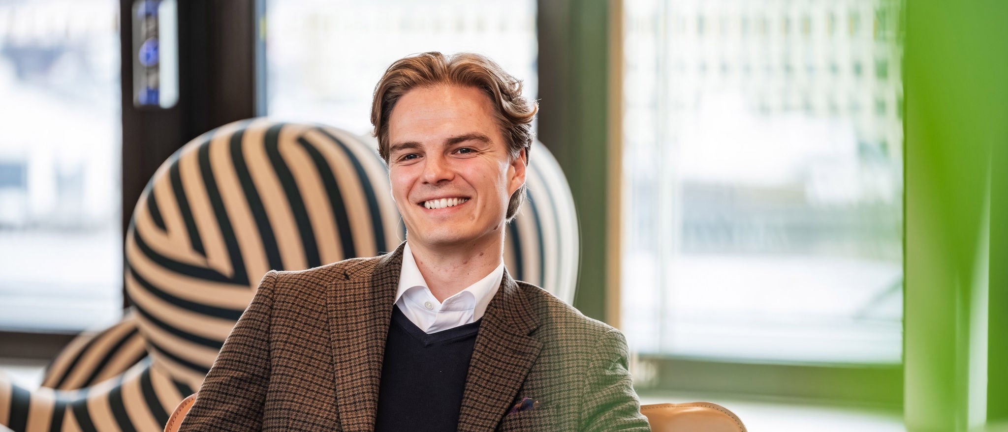 Profesjonell sittende i en lenestol på EY Norges kontor, med store vinduer og moderne kontormøbler i bakgrunnen.