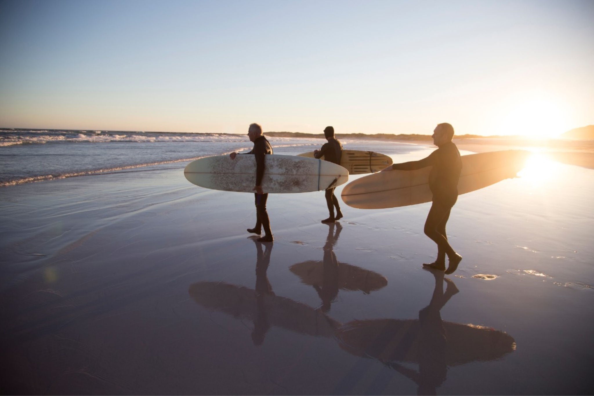 Surfers walking on the beach with surfboards at sunset
