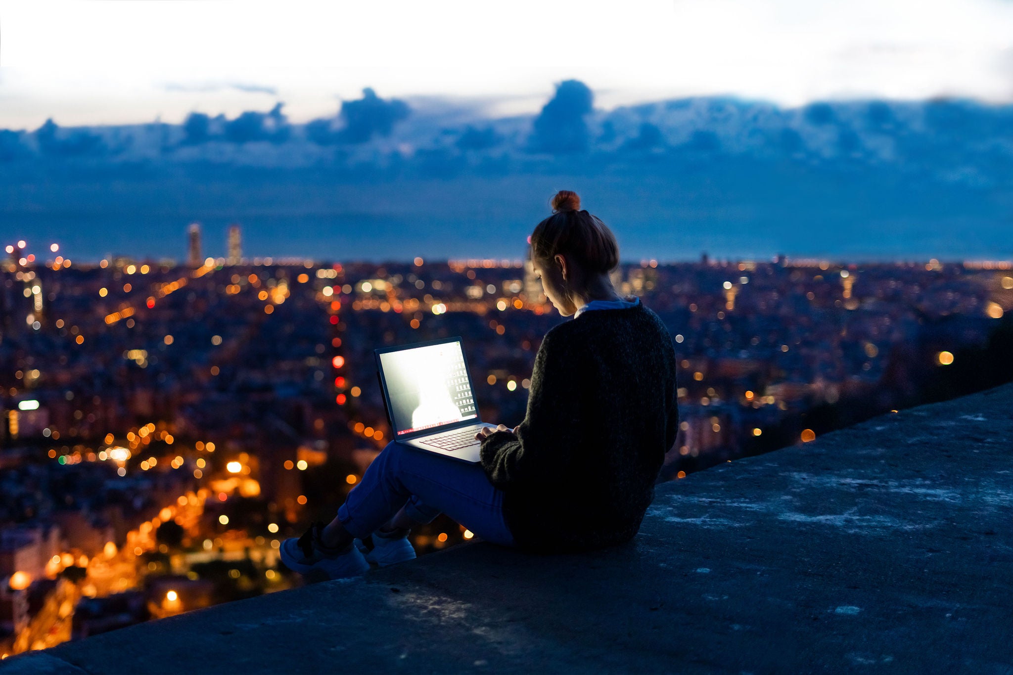 Young woman using laptop at dawn above the city