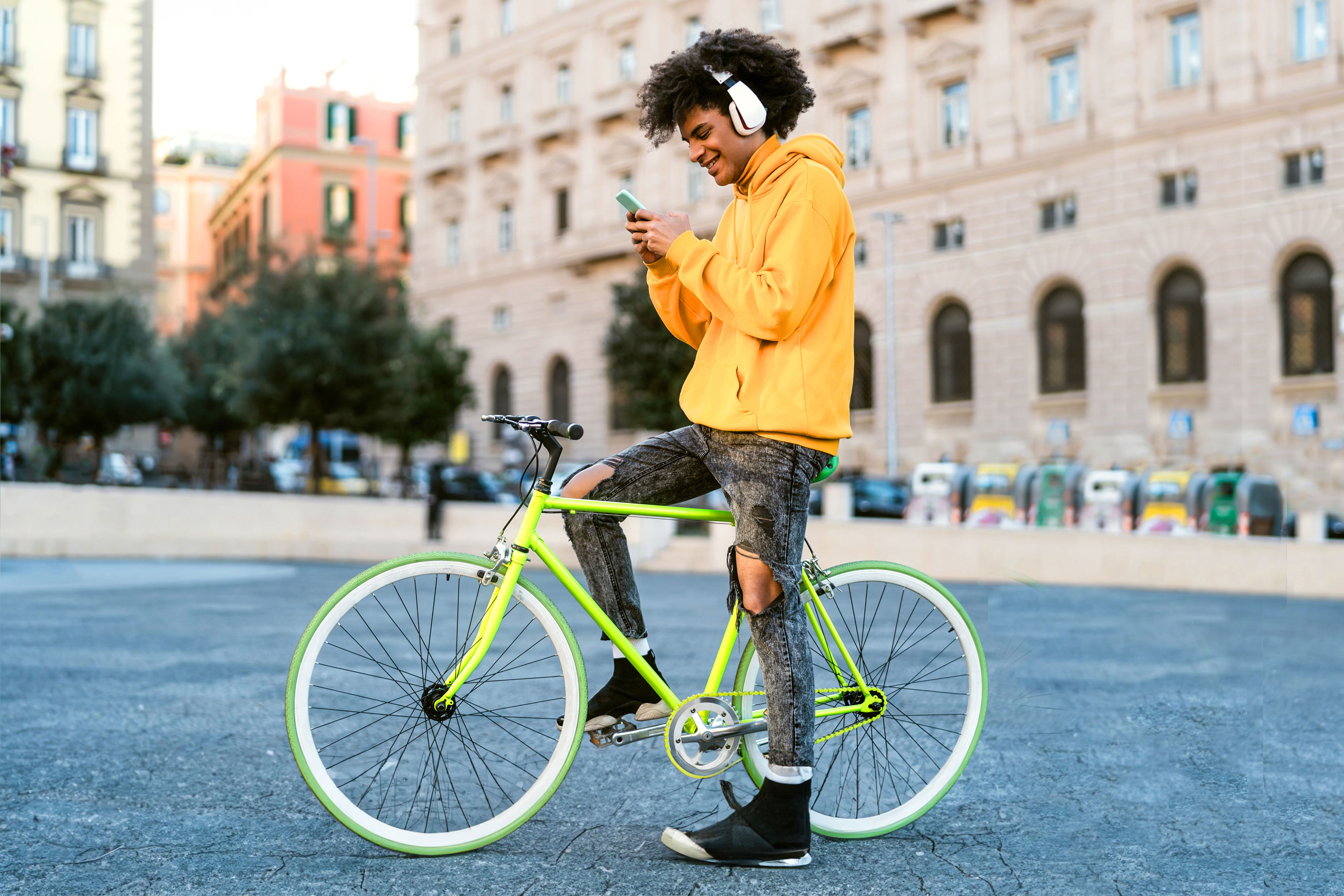Happy African man using mobile smartphone outdoor - Young guy having fun riding with bike in the city - Youth millennial generation lifestyle and technology concept