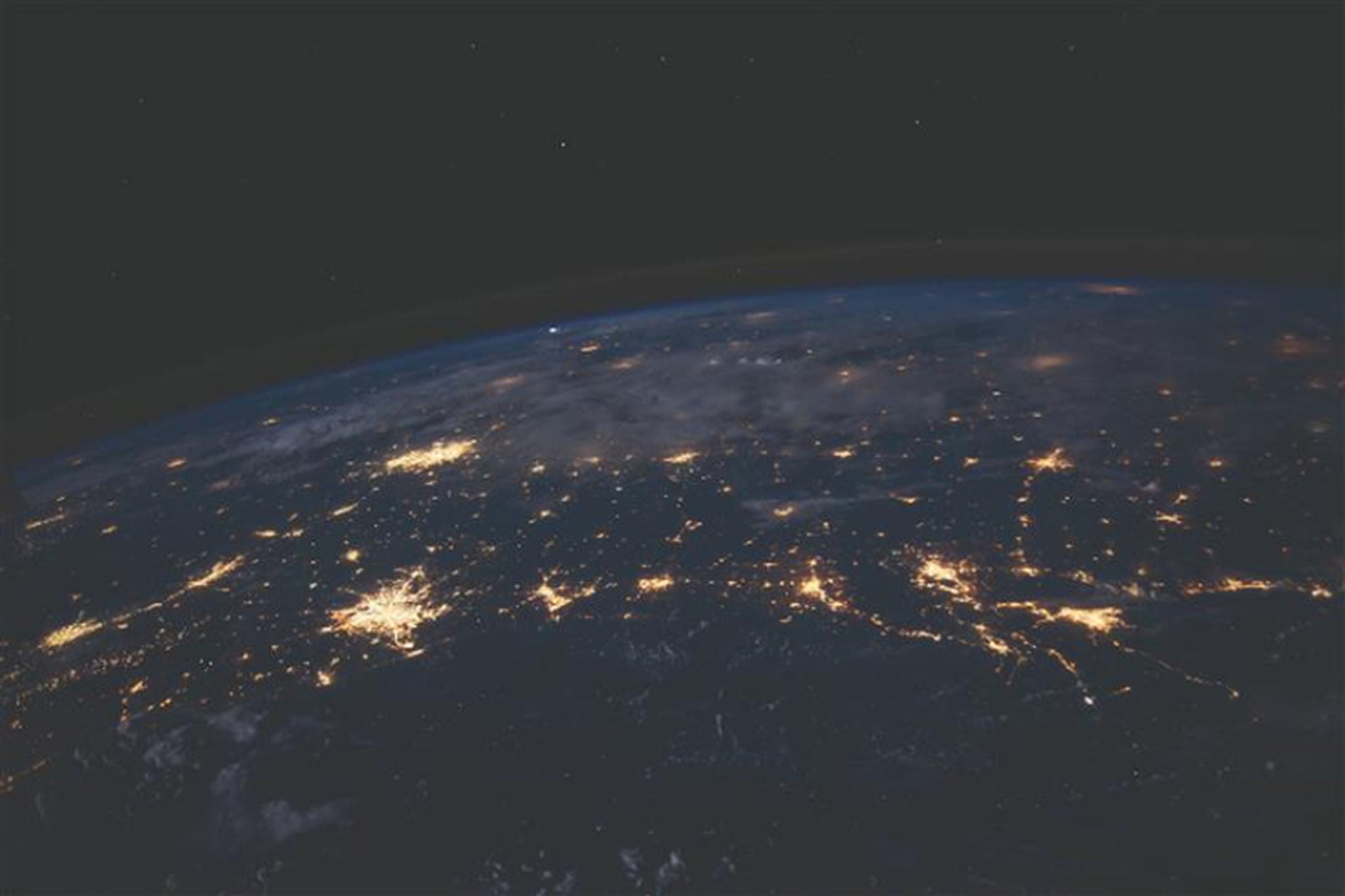 Blick aus dem Weltraum auf die Erde bei Nacht mit leuchtenden Städten und Kontinenten.