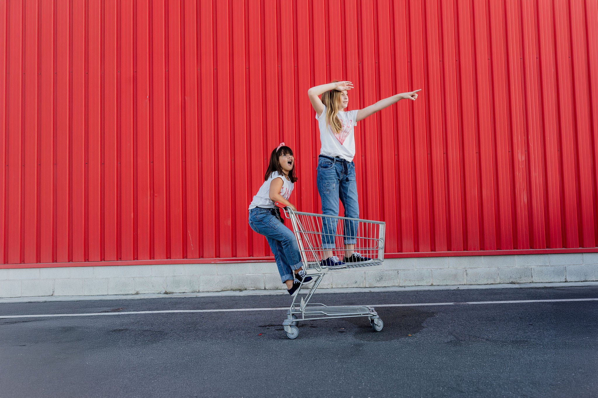 Deux personnes debout sur un chariot devant un grand mur rouge.
