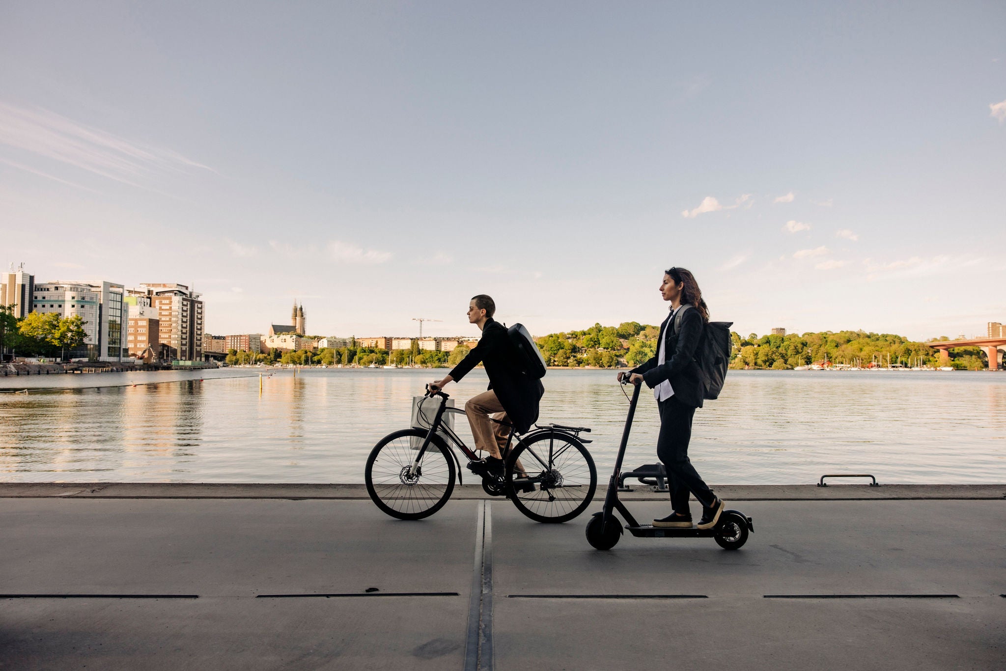 Business people riding electric scooter and bicycle on promenade against sky