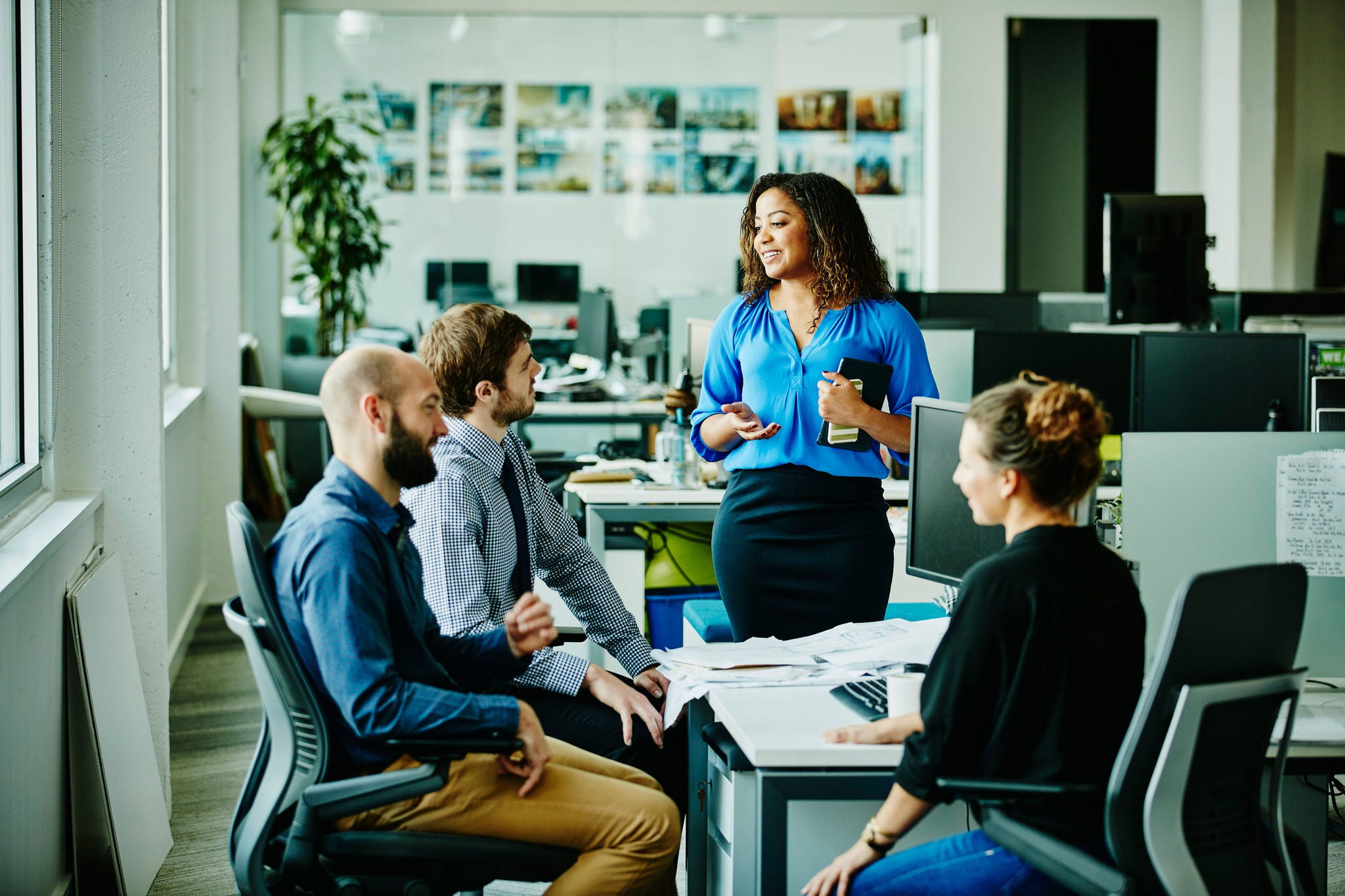 Businesswoman leading informal meeting with colleagues at office workstation